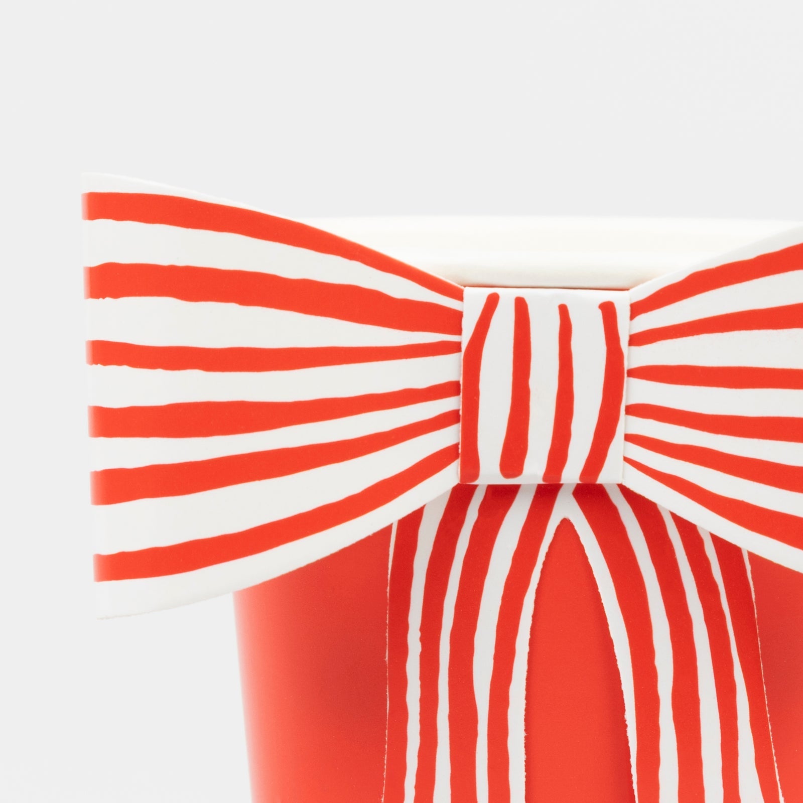 A red paper cup by Meri Meri with a white and red striped paper bow on it.
