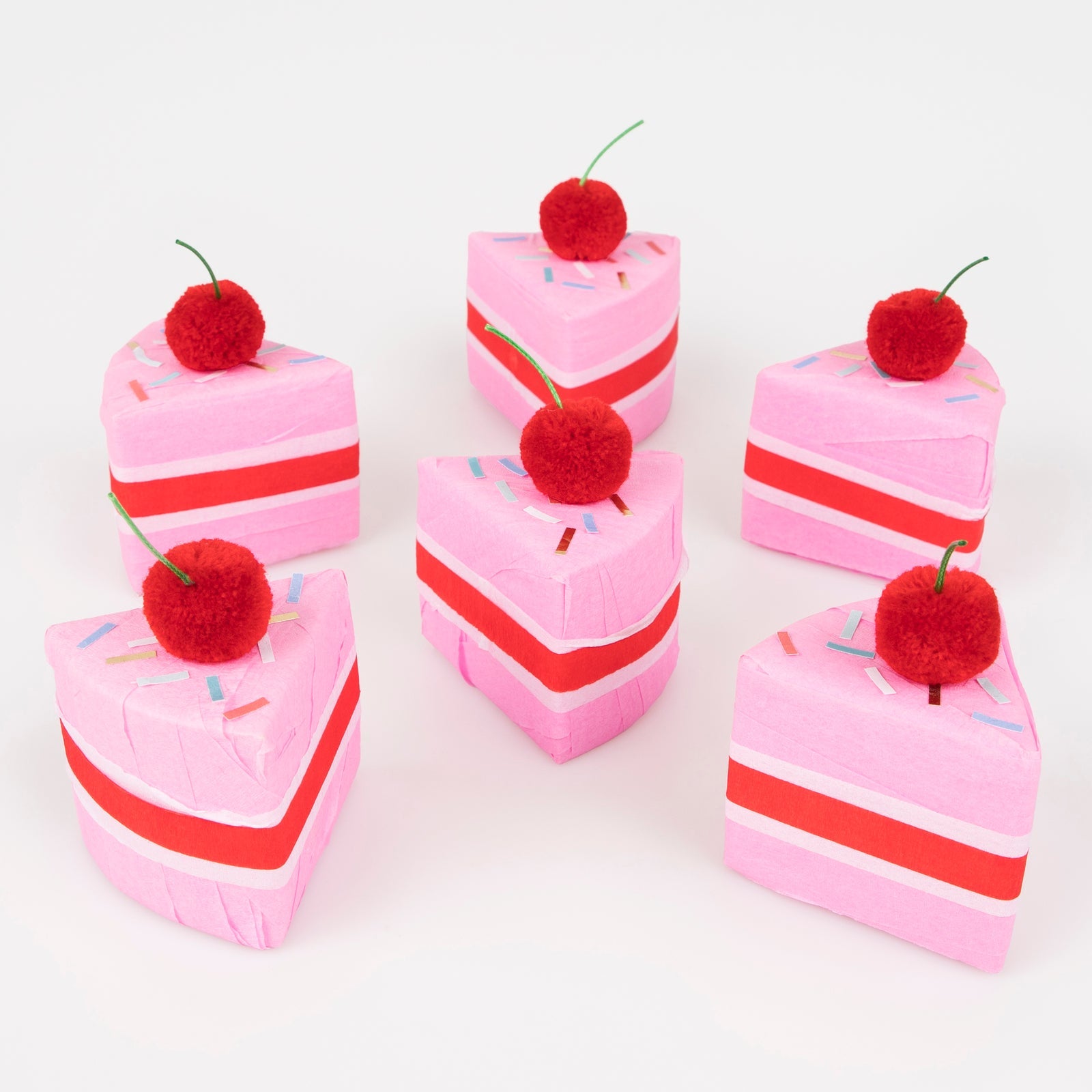 Meri Meri Surprise Cake Slices. A box of 6 cakes slices crafted with red, white and pink crepe paper. Each slice is topped with a red pompom cherry with a green cord stalk, and sprinkle stickers.