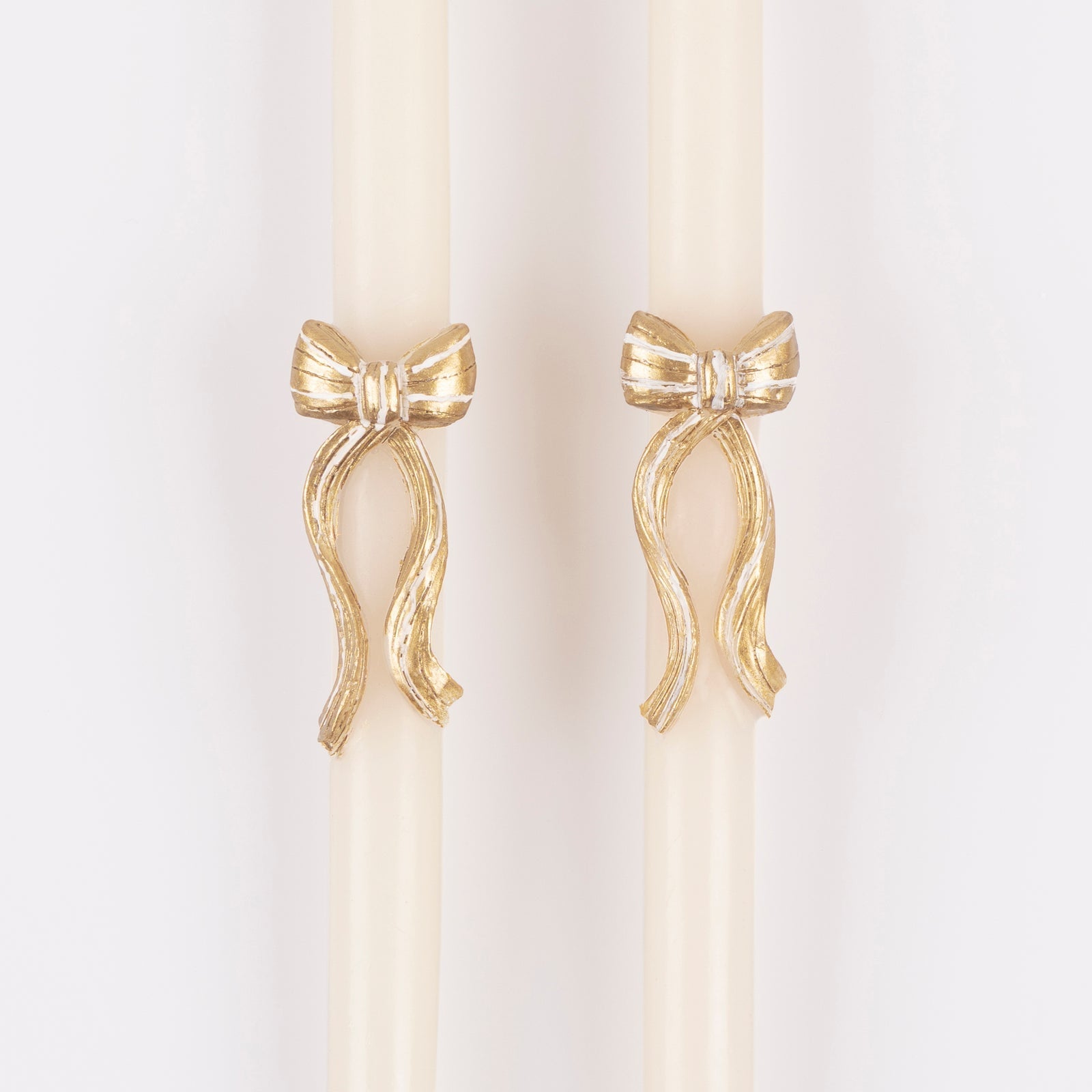 Close up of the gold bow embellishment on two white taper candles.