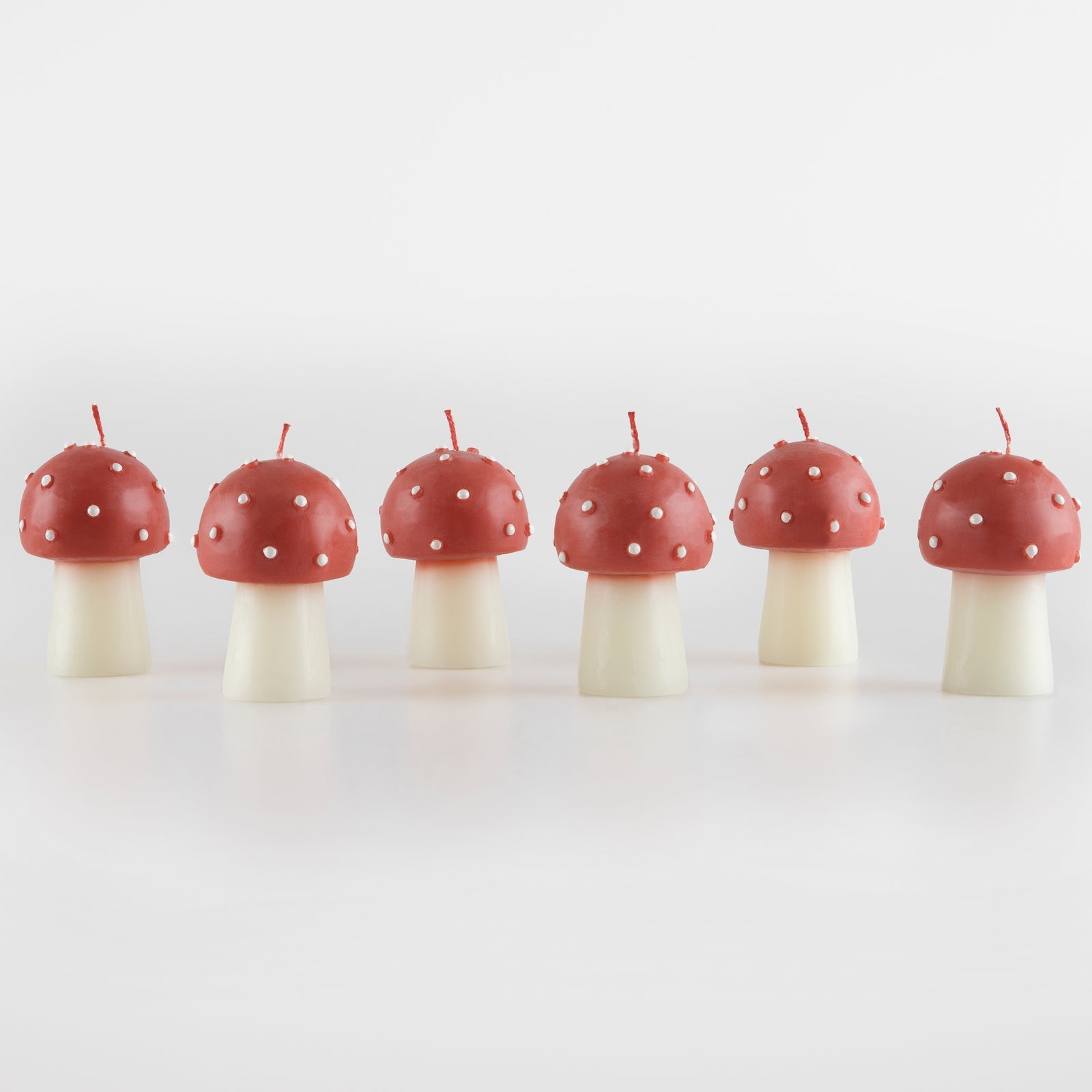 Six red mushroom-shaped candles with white spots on a white background.