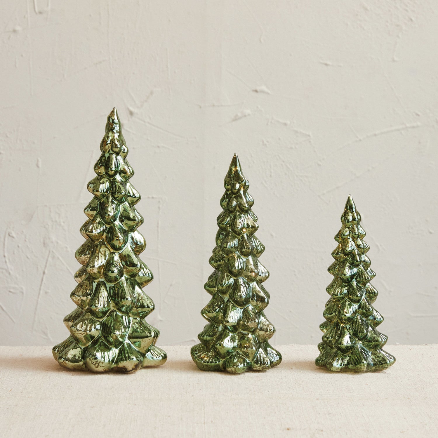 Three green ceramic Christmas trees on a beige surface with a light background
