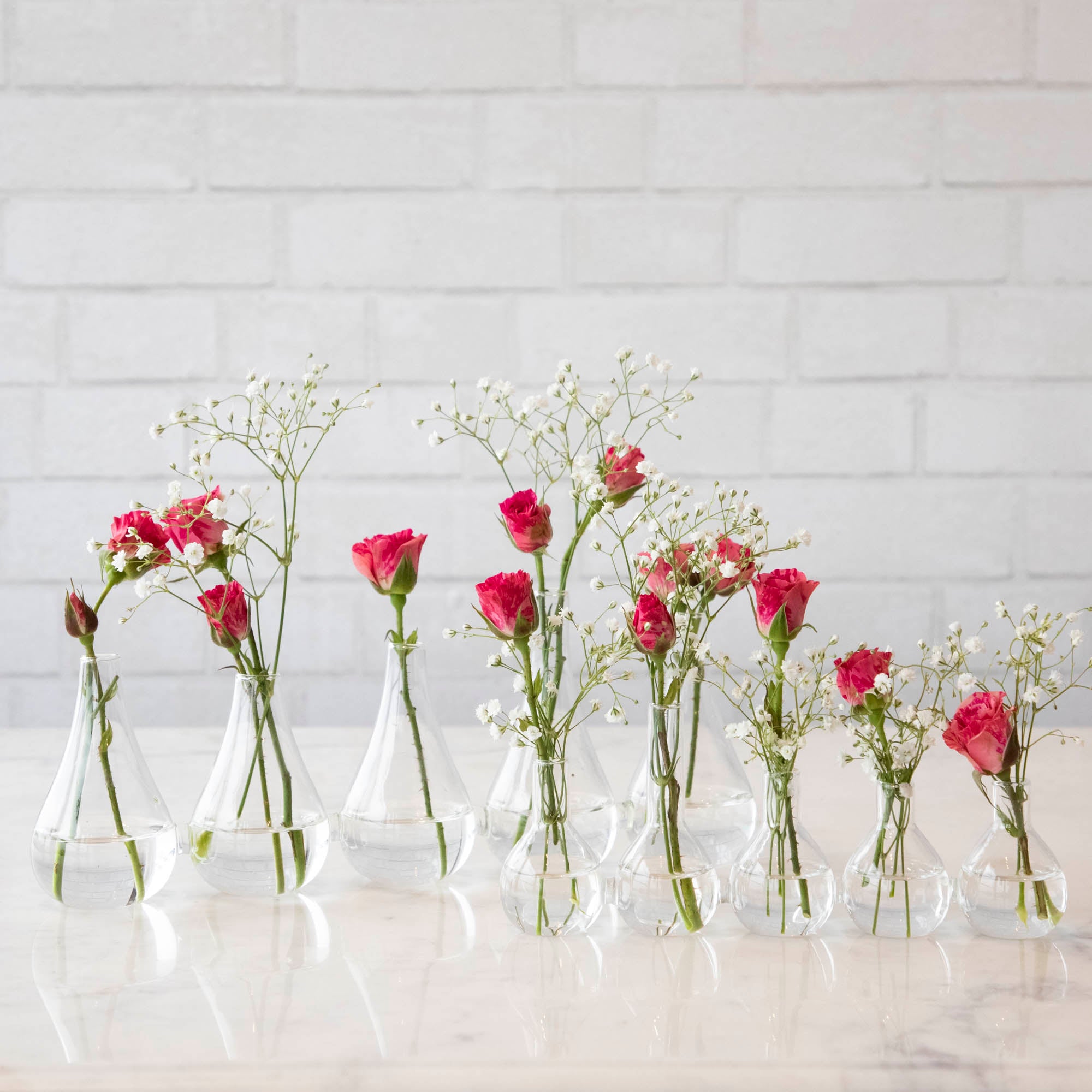 Five Quintet Glass Vases of varying shapes holding floral cuttings of pink roses and baby&
