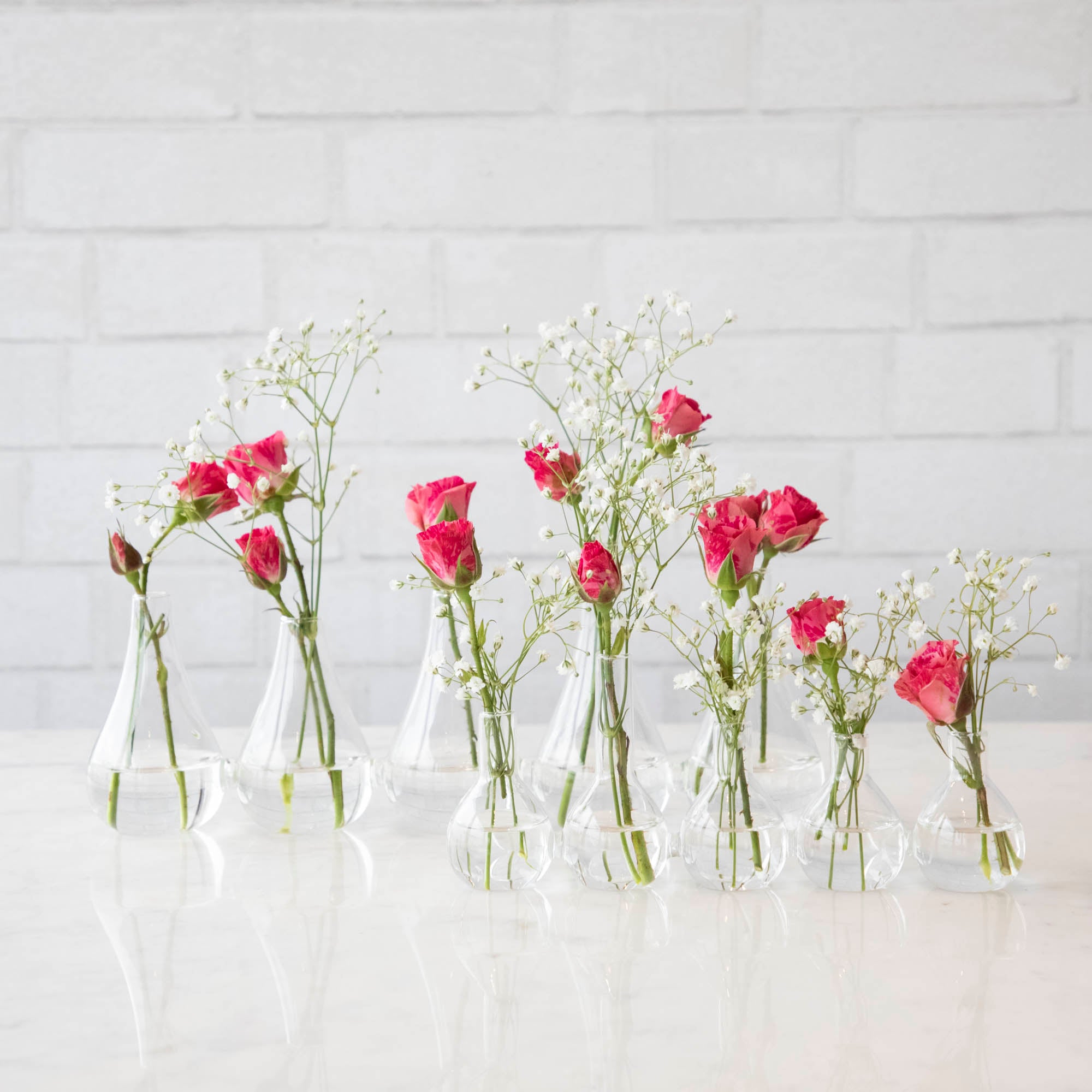 Five Quintet Glass Vases of varying shapes holding floral cuttings of pink roses and baby&