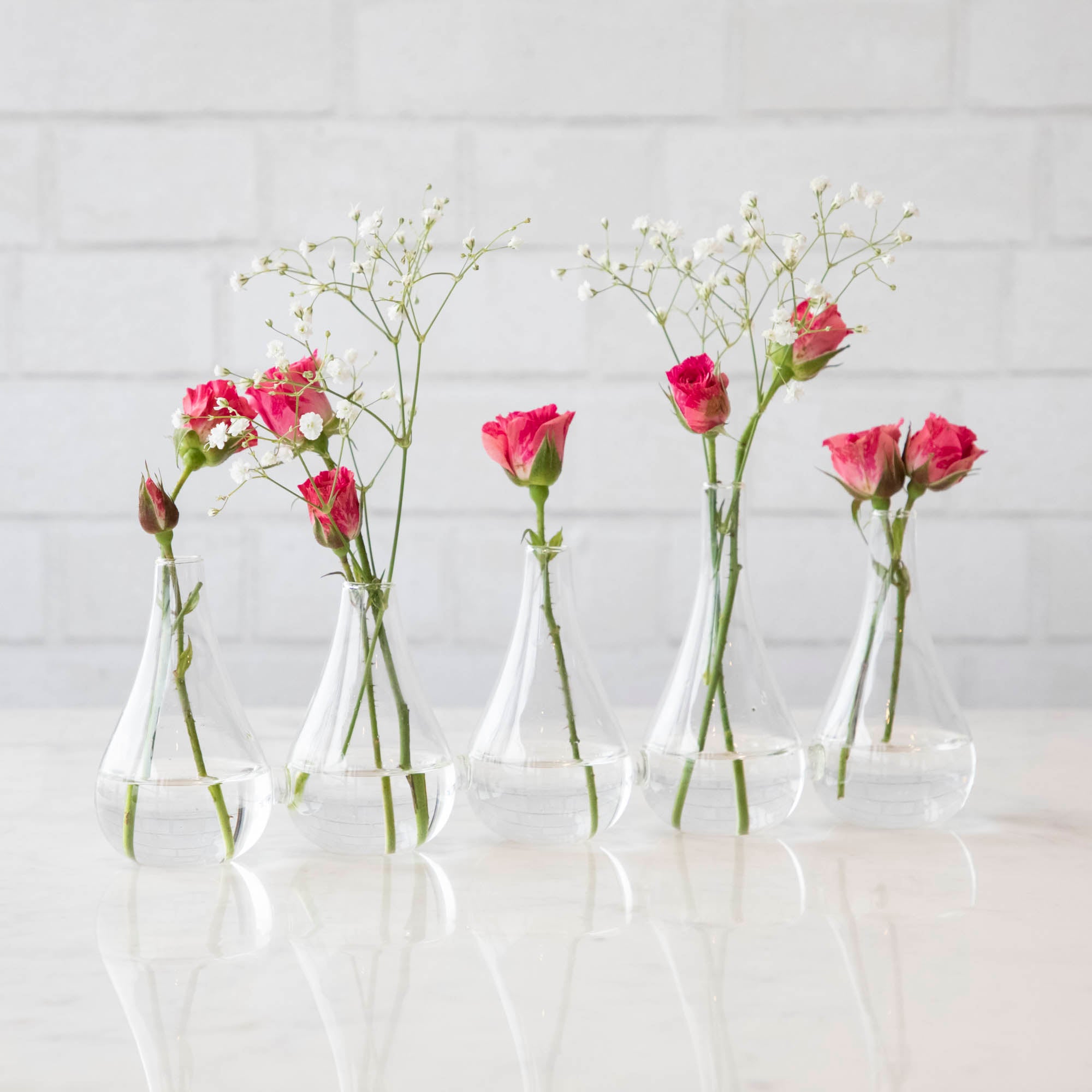 Five Quintet Glass Vases of varying shapes holding floral cuttings of pink roses and baby&