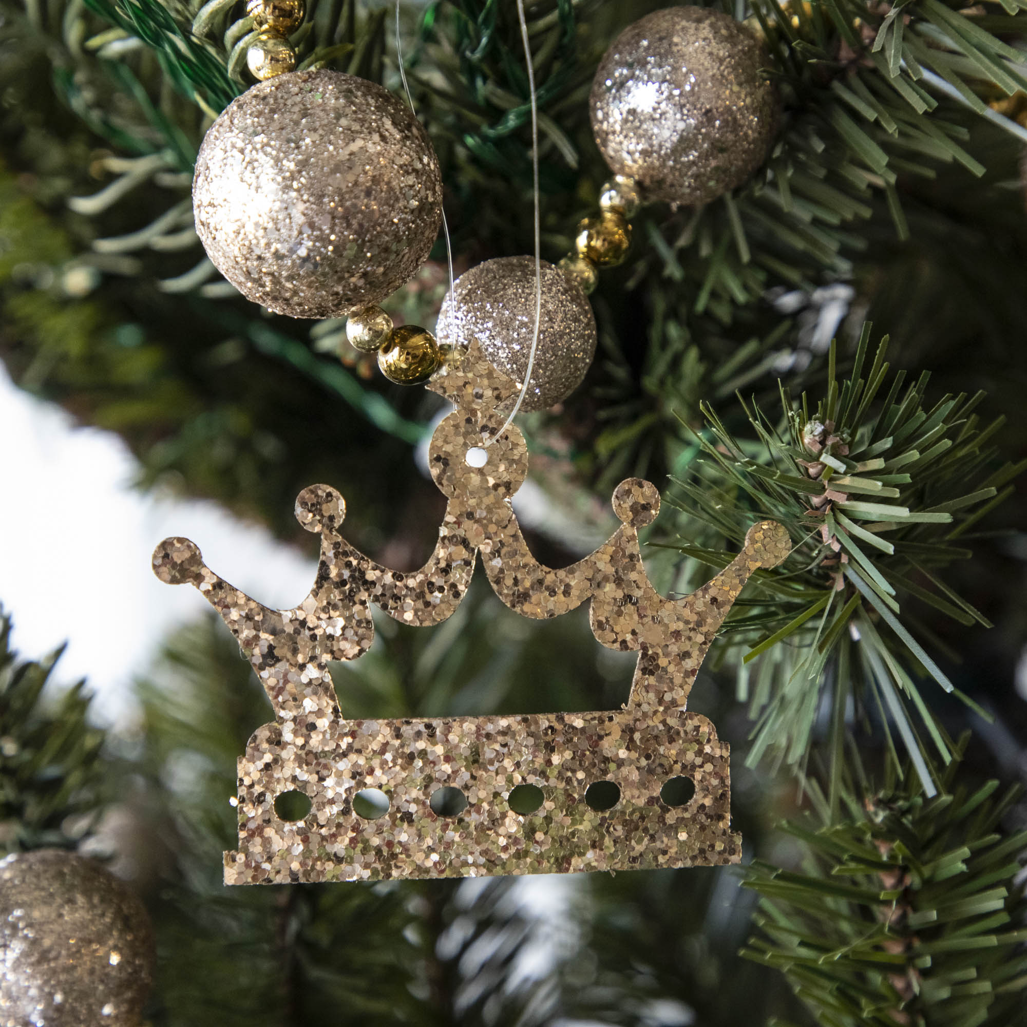 Gold glitter crown-shaped ornament hanging on a Christmas tree.