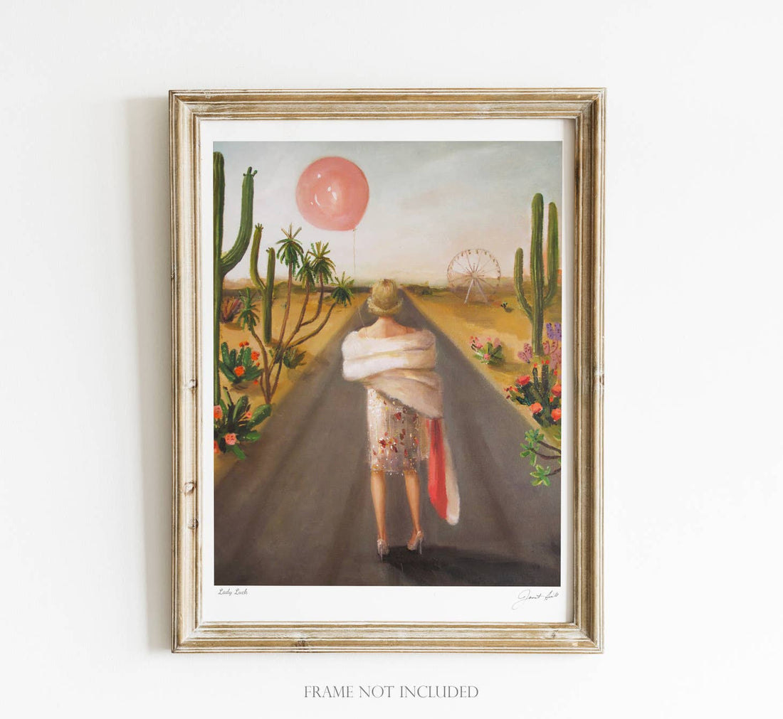 A framed surrealist painting by fine artist Janet Hill of a person standing in a desert landscape with cacti and a small ferris wheel, gazing at a floating pink balloon. Janet Hill&