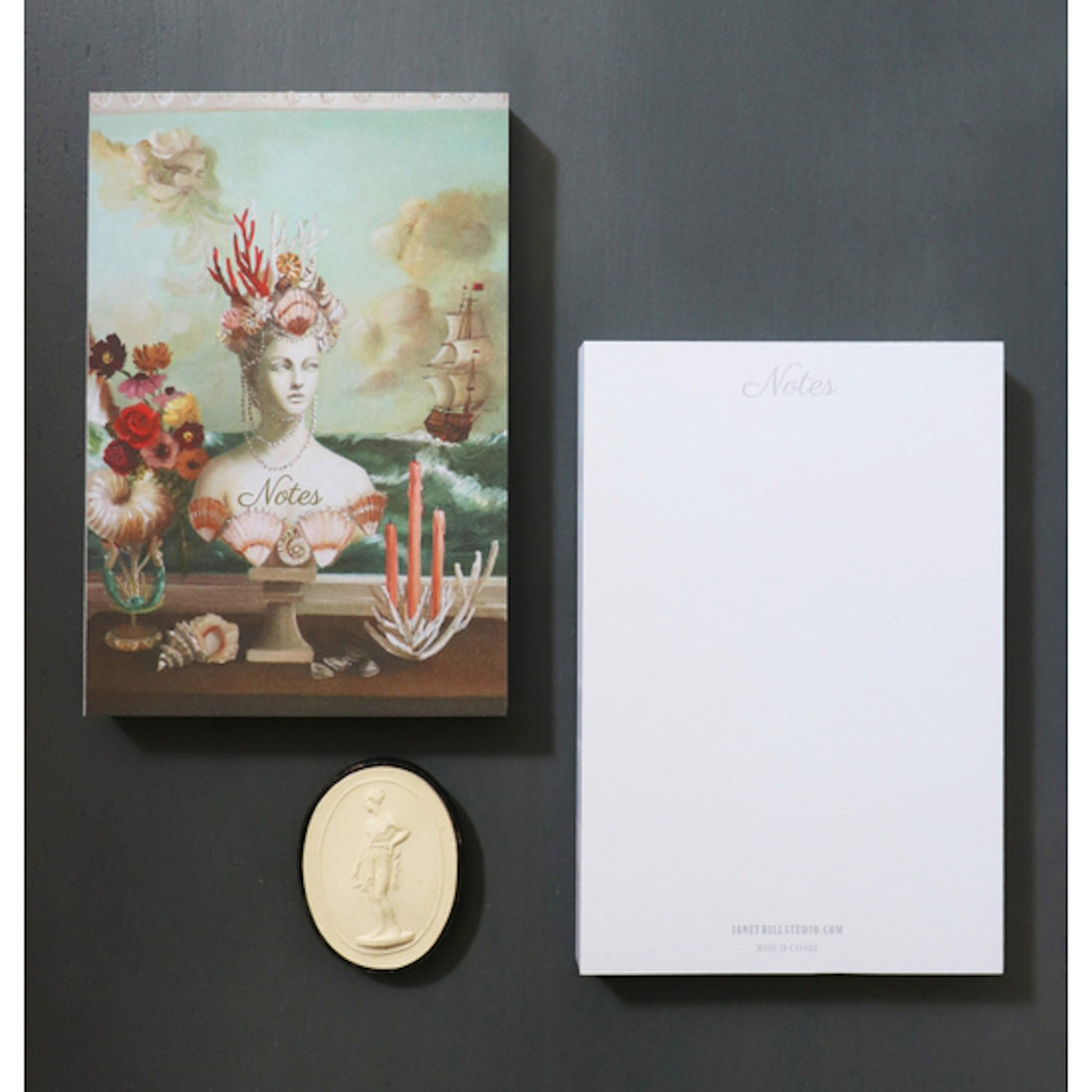 &quot;The Gods&quot; Tear-Away Notepad resting on a black table next to a single sheet flipped over to show the blank white back side labeled &quot;Notes&quot; across the top. The artwork is a painterly illustration of a white marble goddess bust wearing a crown of sea shells and coral, next to a bouquet and tapered candles in front of a painting of a ship at sea.