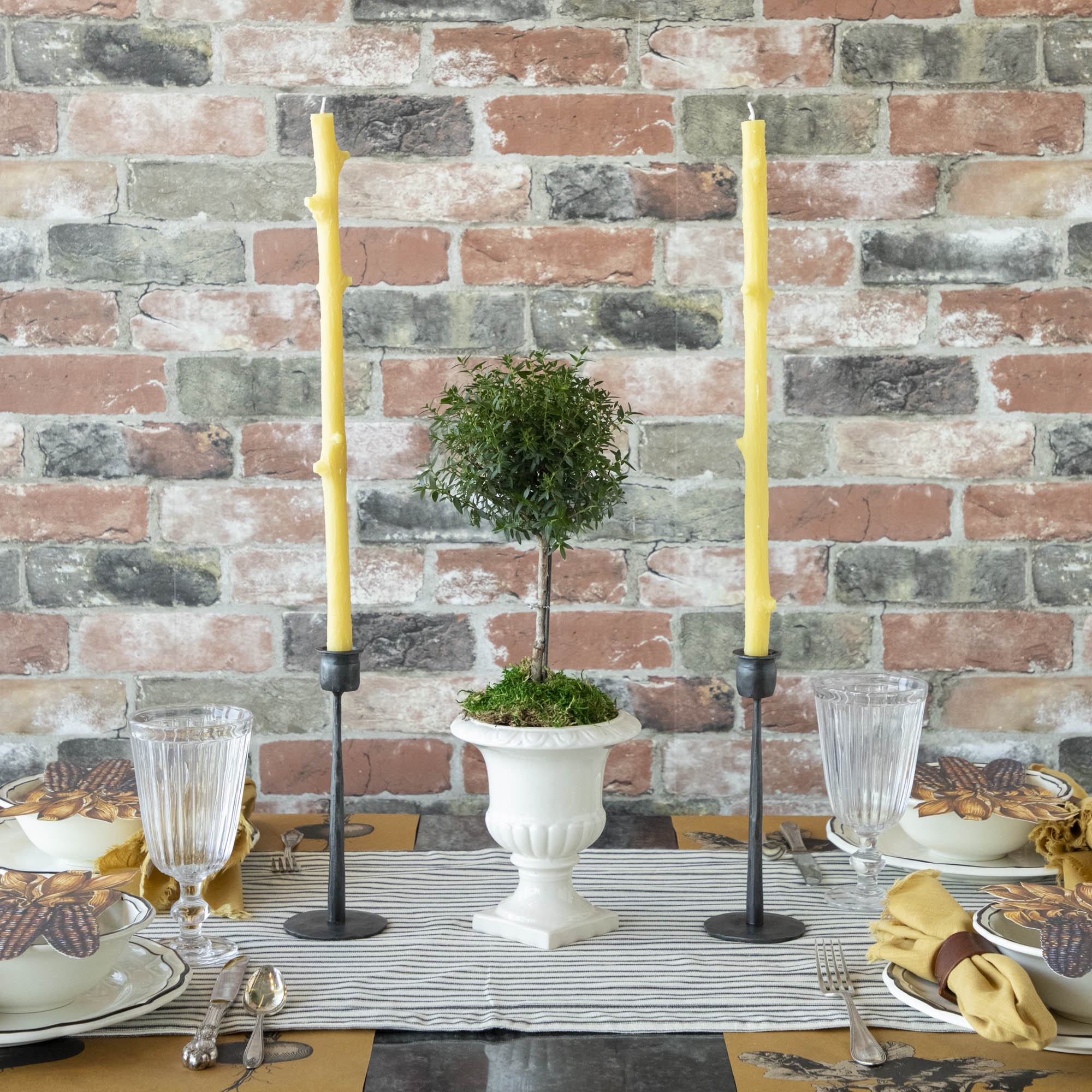 A Stick Candles set and a group of candles on top of a textured brick wall.