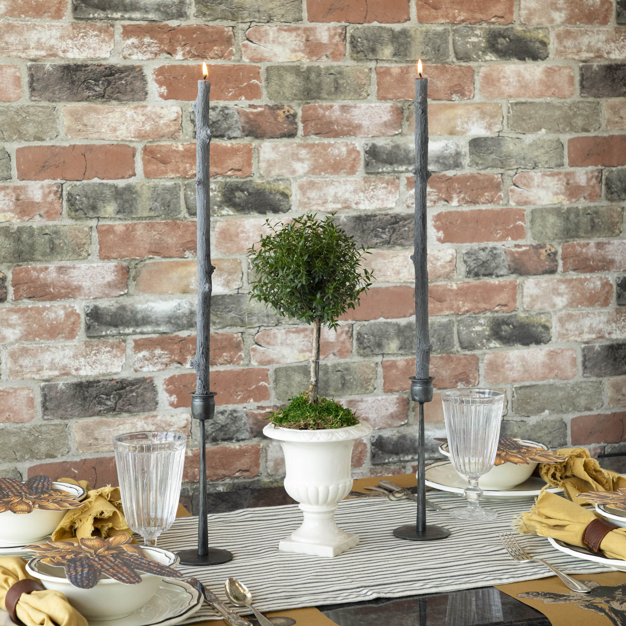 A Stick Candles set and a group of candles on top of a textured brick wall.