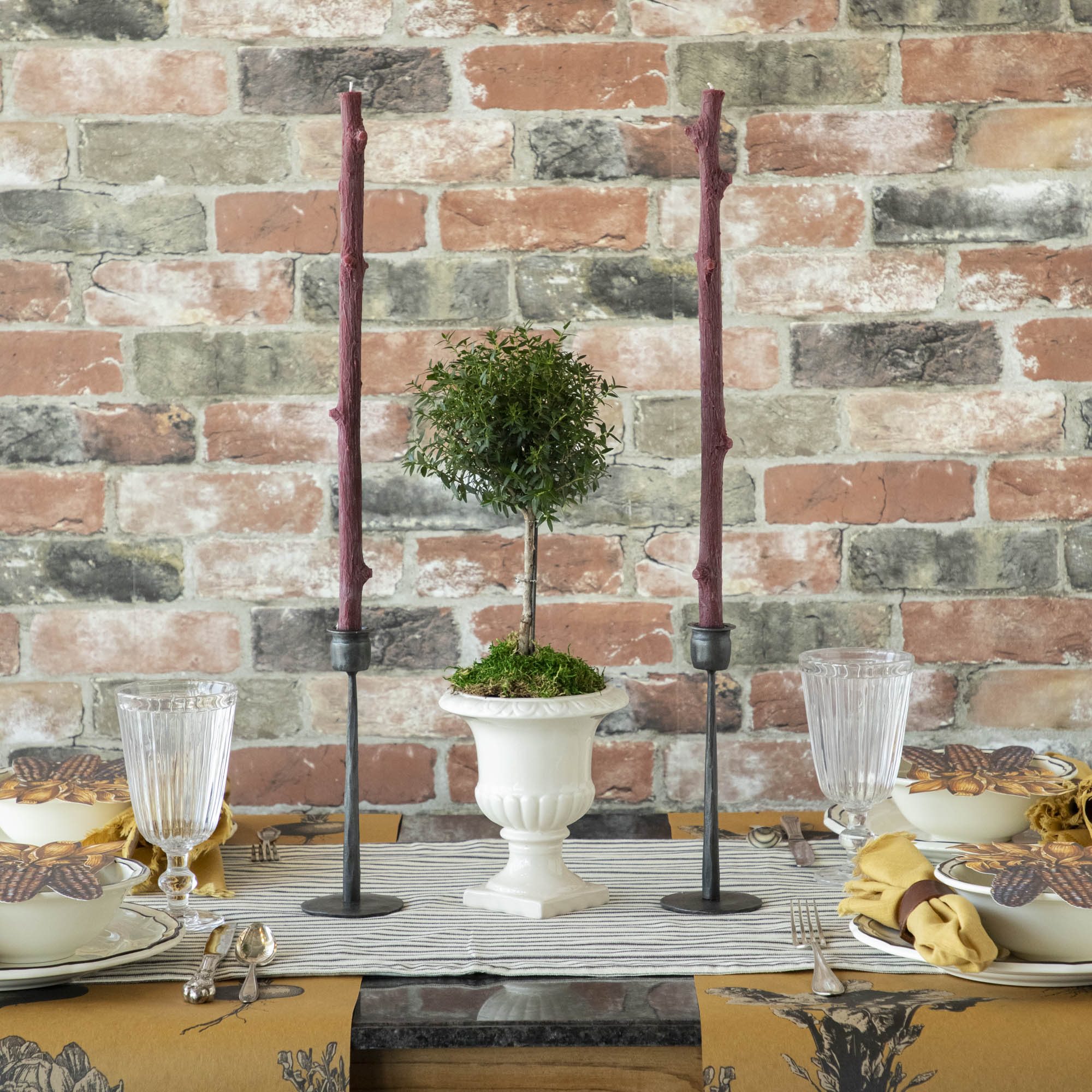 A Stick Candles set and a group of candles on top of a textured brick wall.