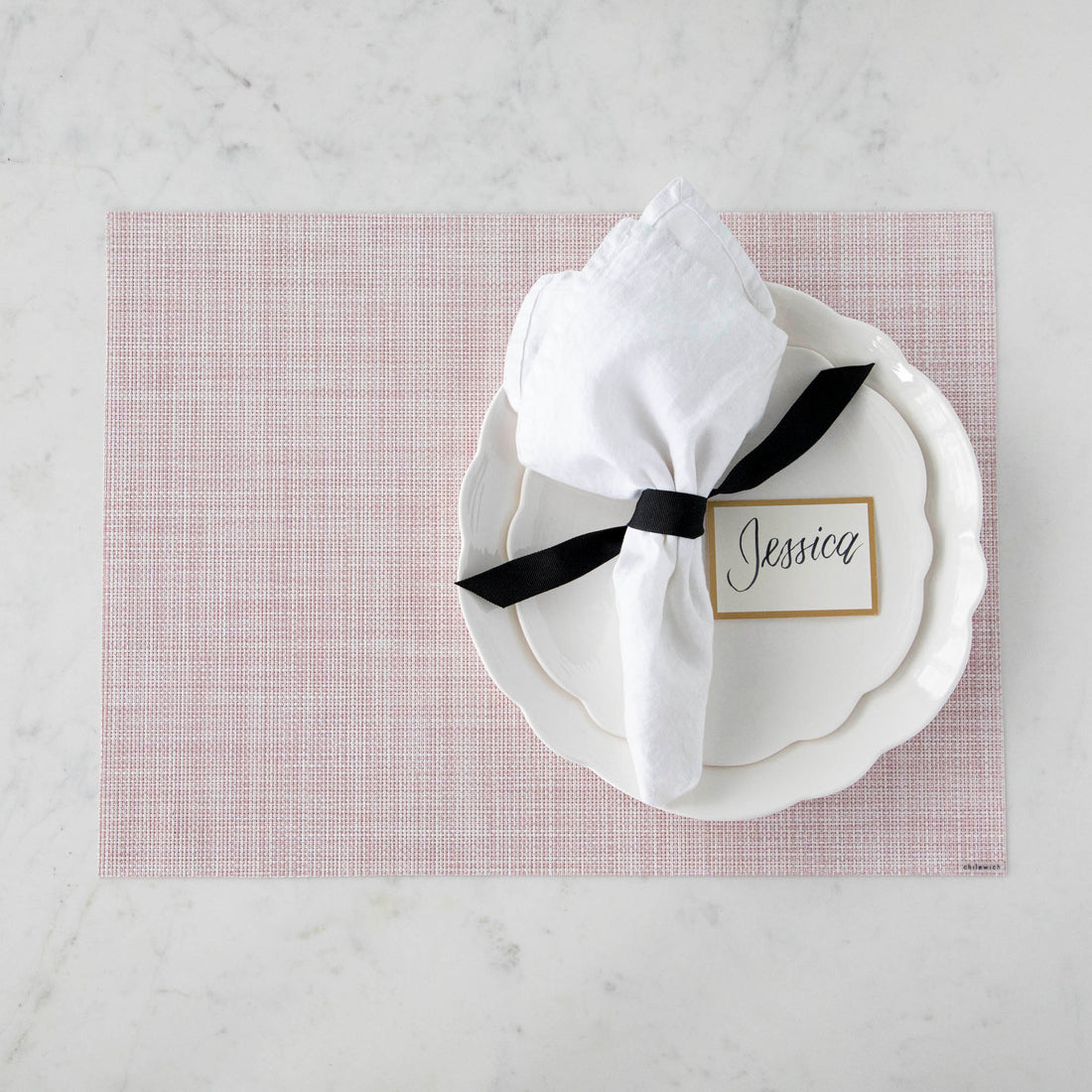Elegant table setting with a floral theme, featuring pink and white dishes, gold cutlery, Chilewich Blush Mini Basketweave Mats, and personalized name card.