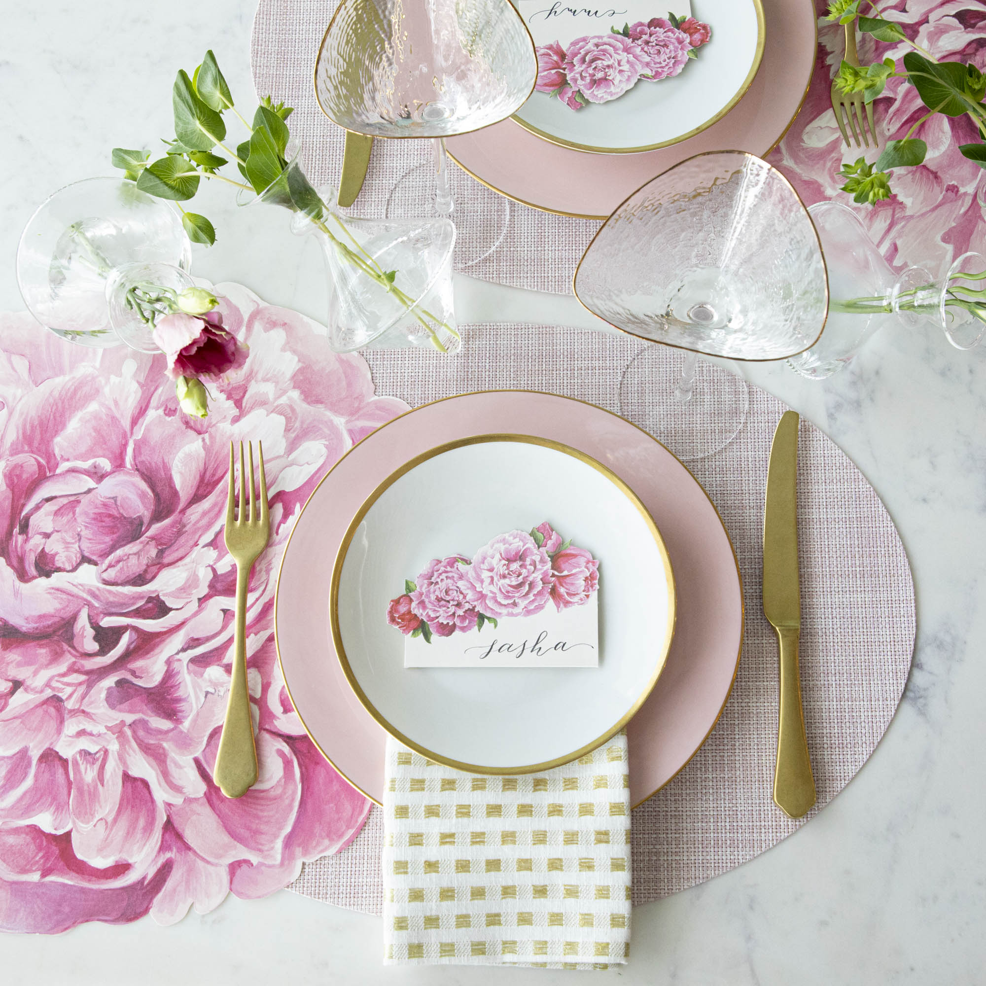 Elegant table setting with a floral theme, featuring pink and white dishes, gold cutlery, Chilewich Blush Mini Basketweave Mats, and personalized name card.