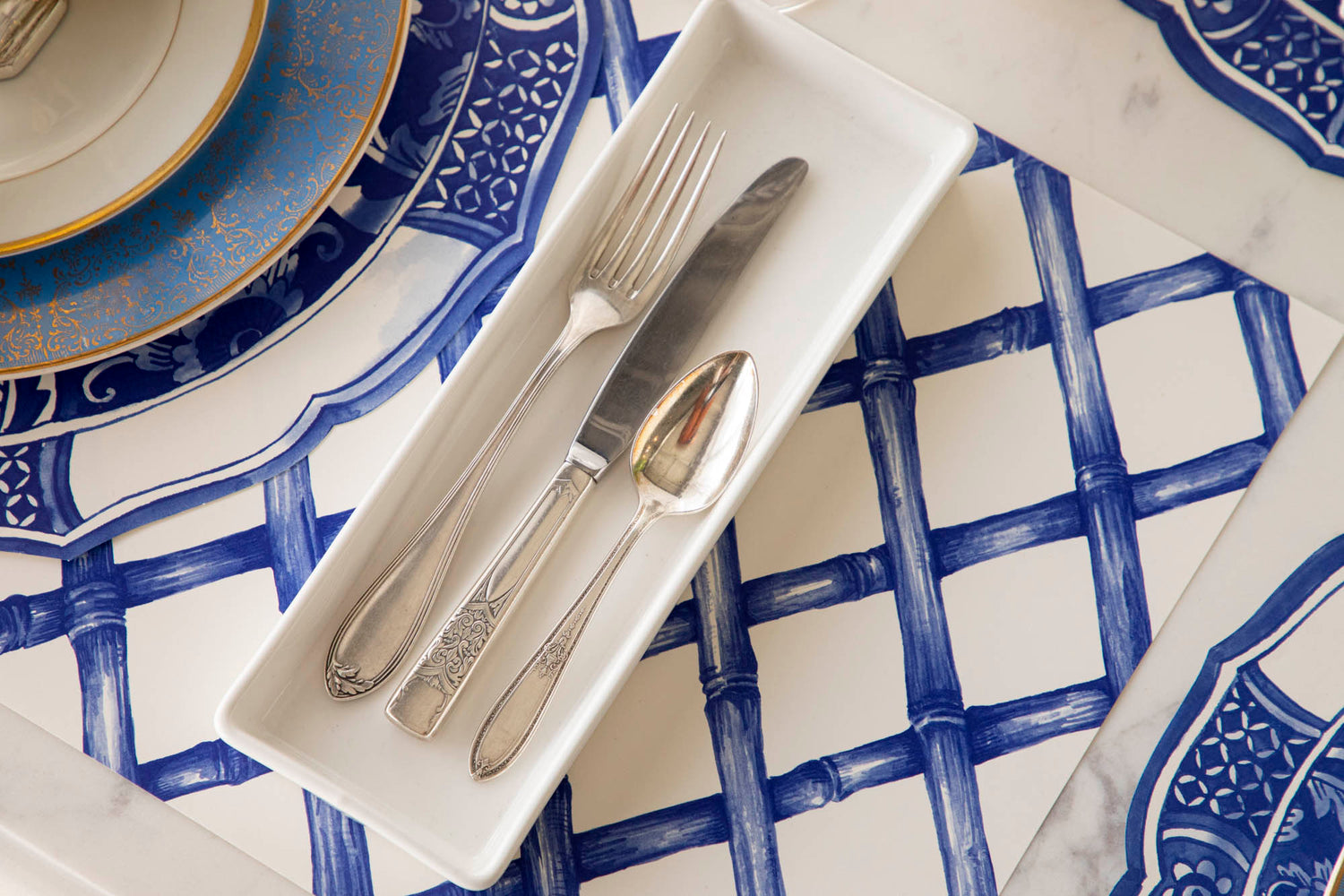 A blue and white table setting with silverware on the Blue Lattice Placemat.