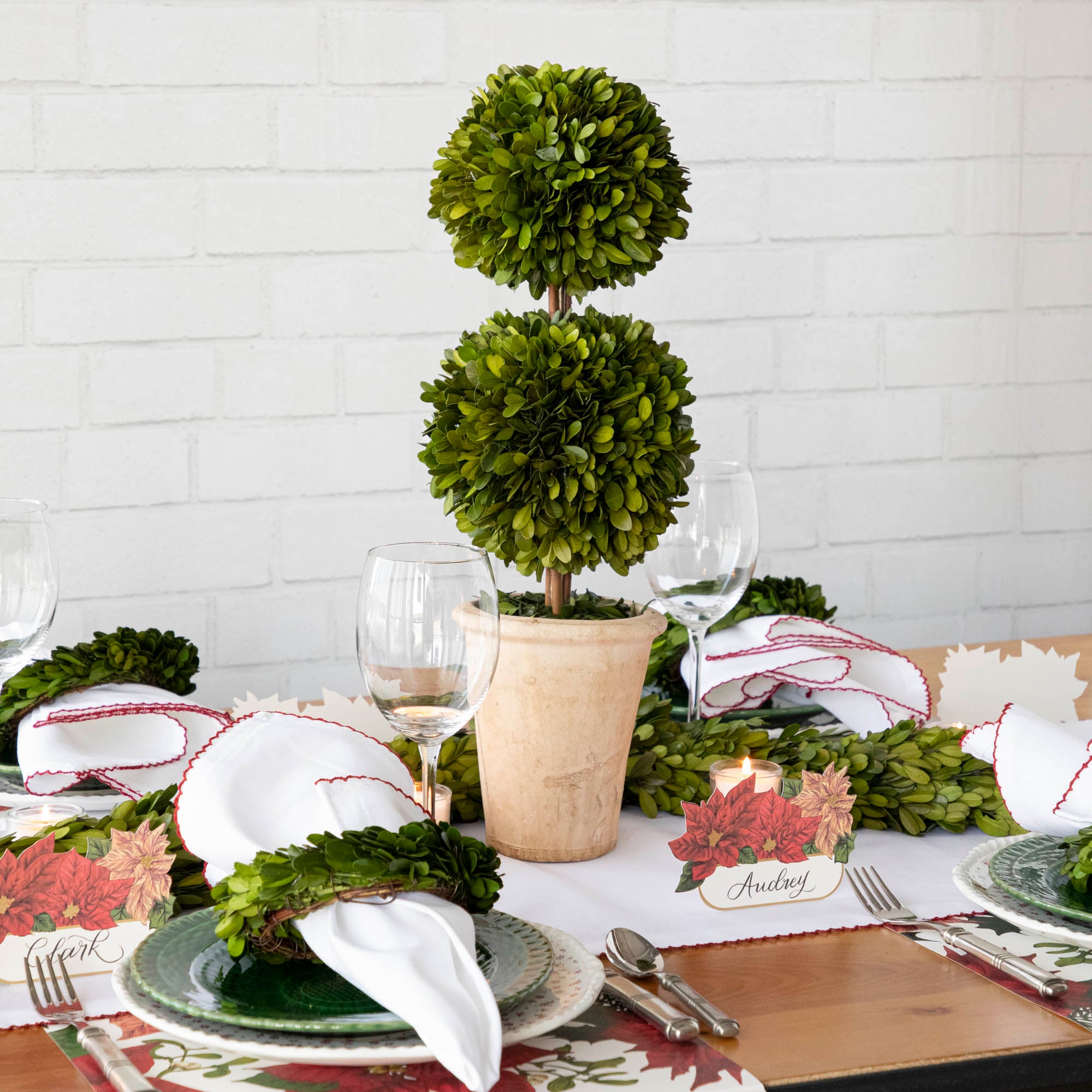 A Christmas table setting with a Mills Floral Company Preserved Boxwood Double Ball Topiary in a pot.