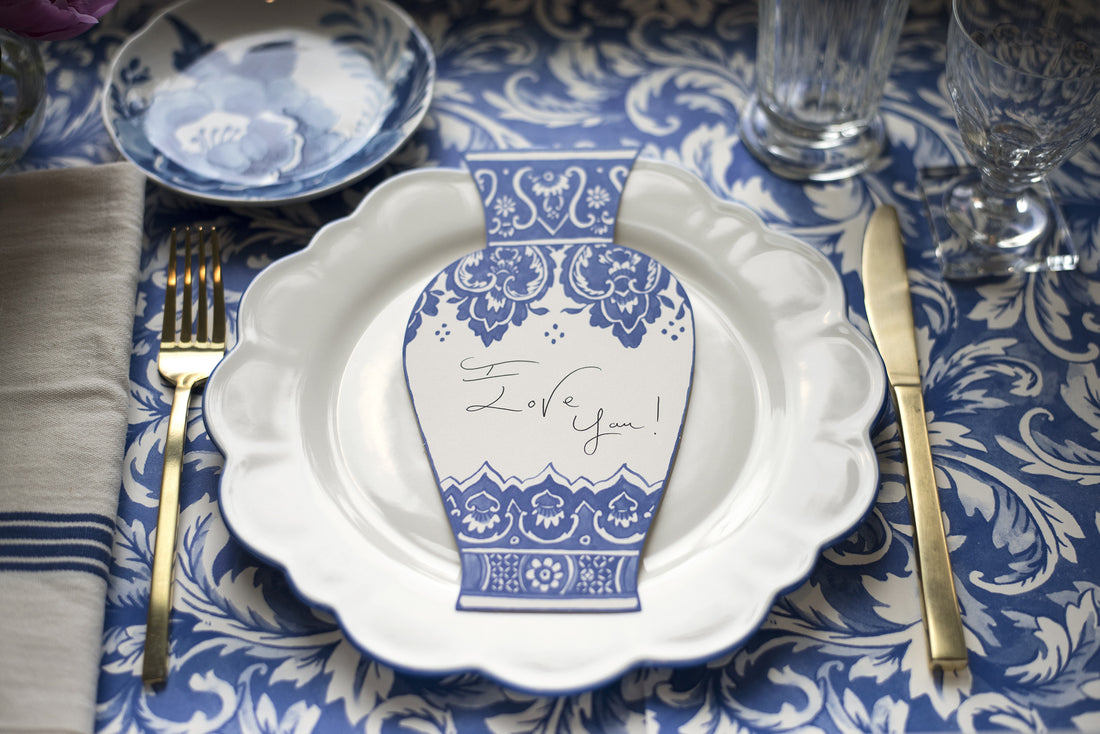 An elegant floral place setting featuring a China Blue Vase Table Accent with &quot;I Love You!&quot; written on it resting on the plate.