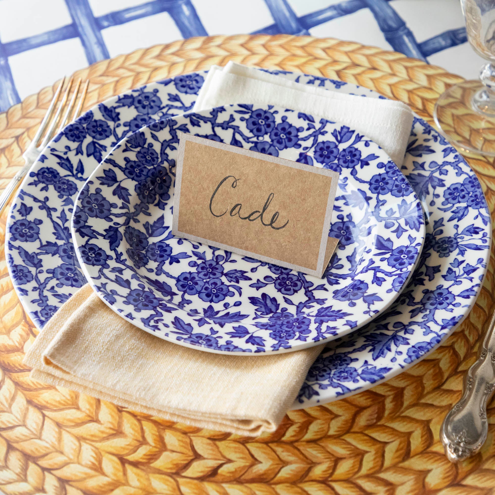 A Burleigh Blue Arden dinnerware plate on a wicker placemat with a folded napkin and a fork to the side, also noted as dishwasher safe.