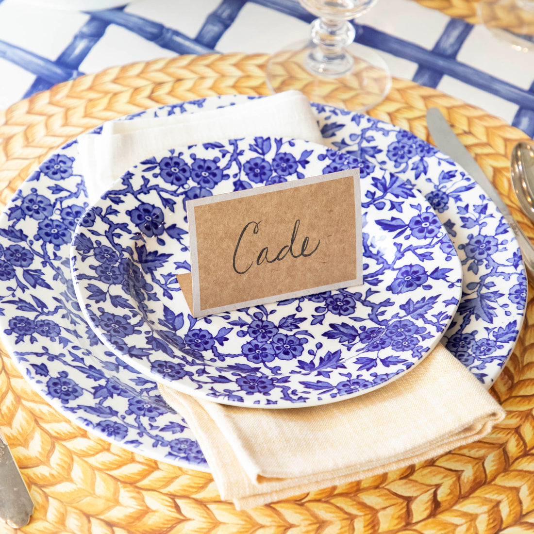 An elegant place setting featuring a Kraft White Frame Place Card labeled &quot;Cade&quot; standing on the plate.