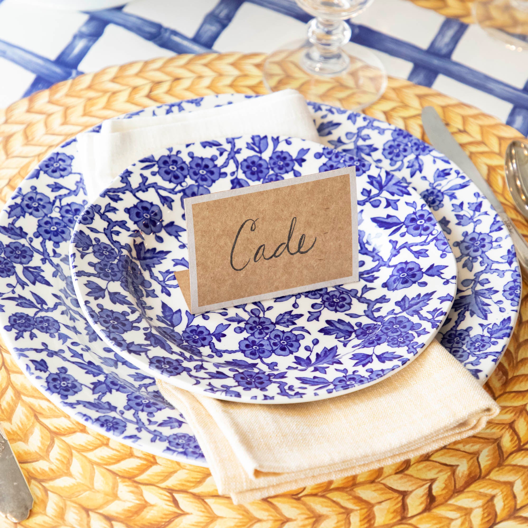 An elegant place setting featuring a Kraft White Frame Place Card labeled "Cade" standing on the plate.