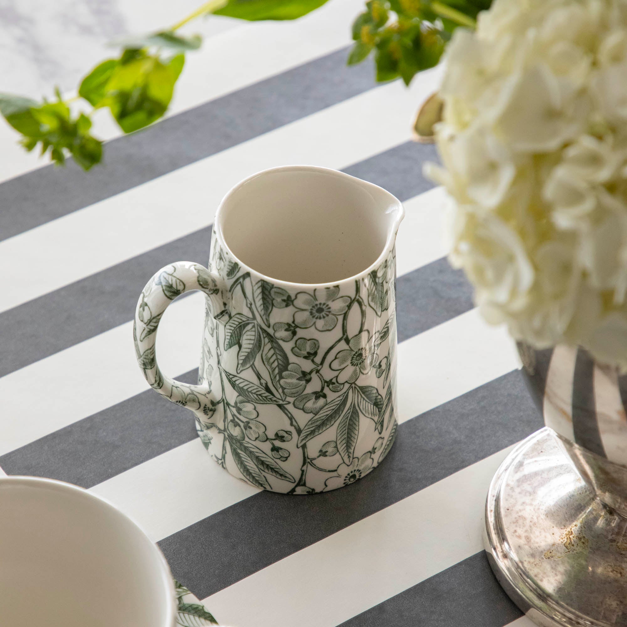 Burleigh Green Prunus Tankard Jug next to a pot of flowers on the Black Classic Stripe Runner.