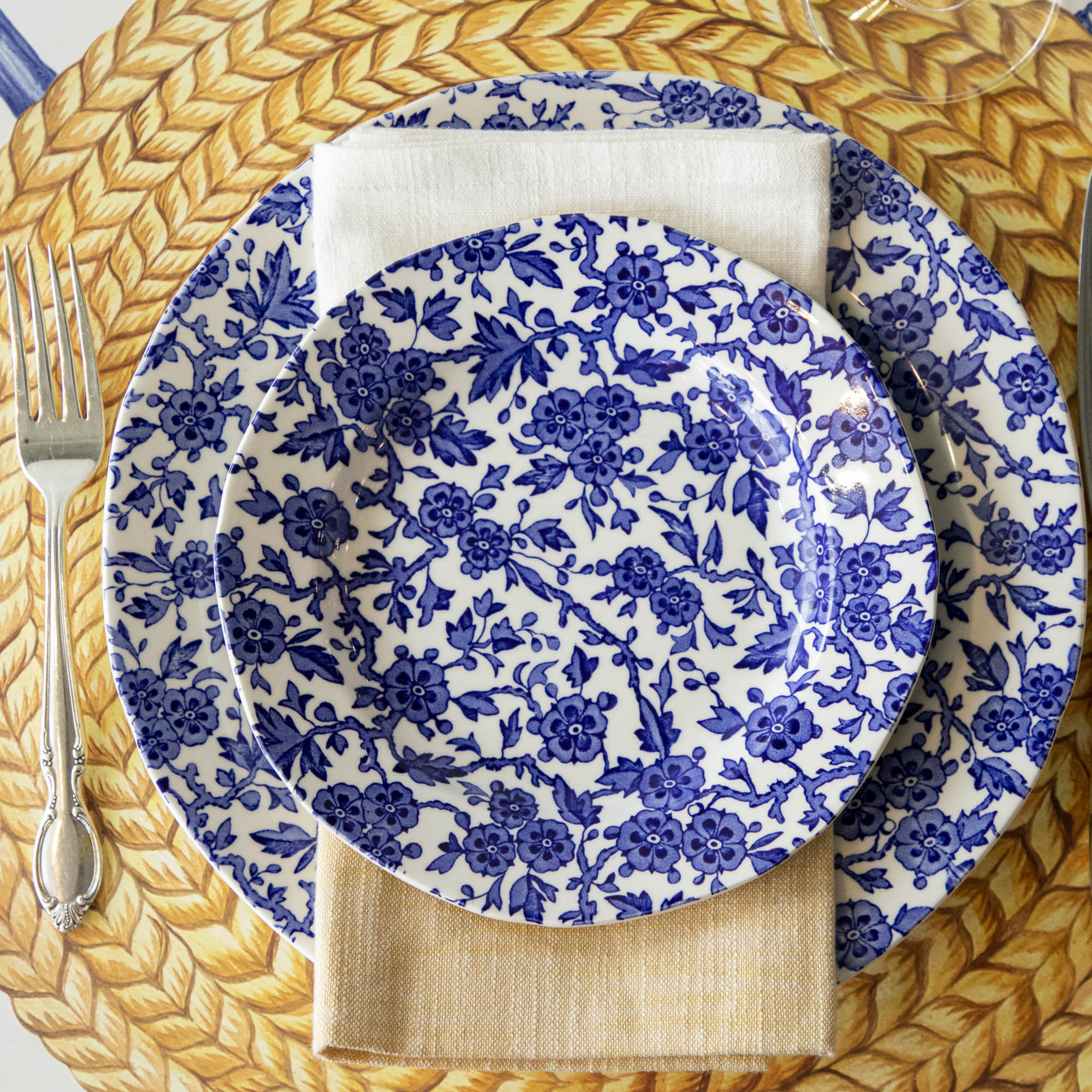 Burleigh Blue Arden plates on the Die-cut Braided Jute placemat with a folded napkin and a fork to the side.