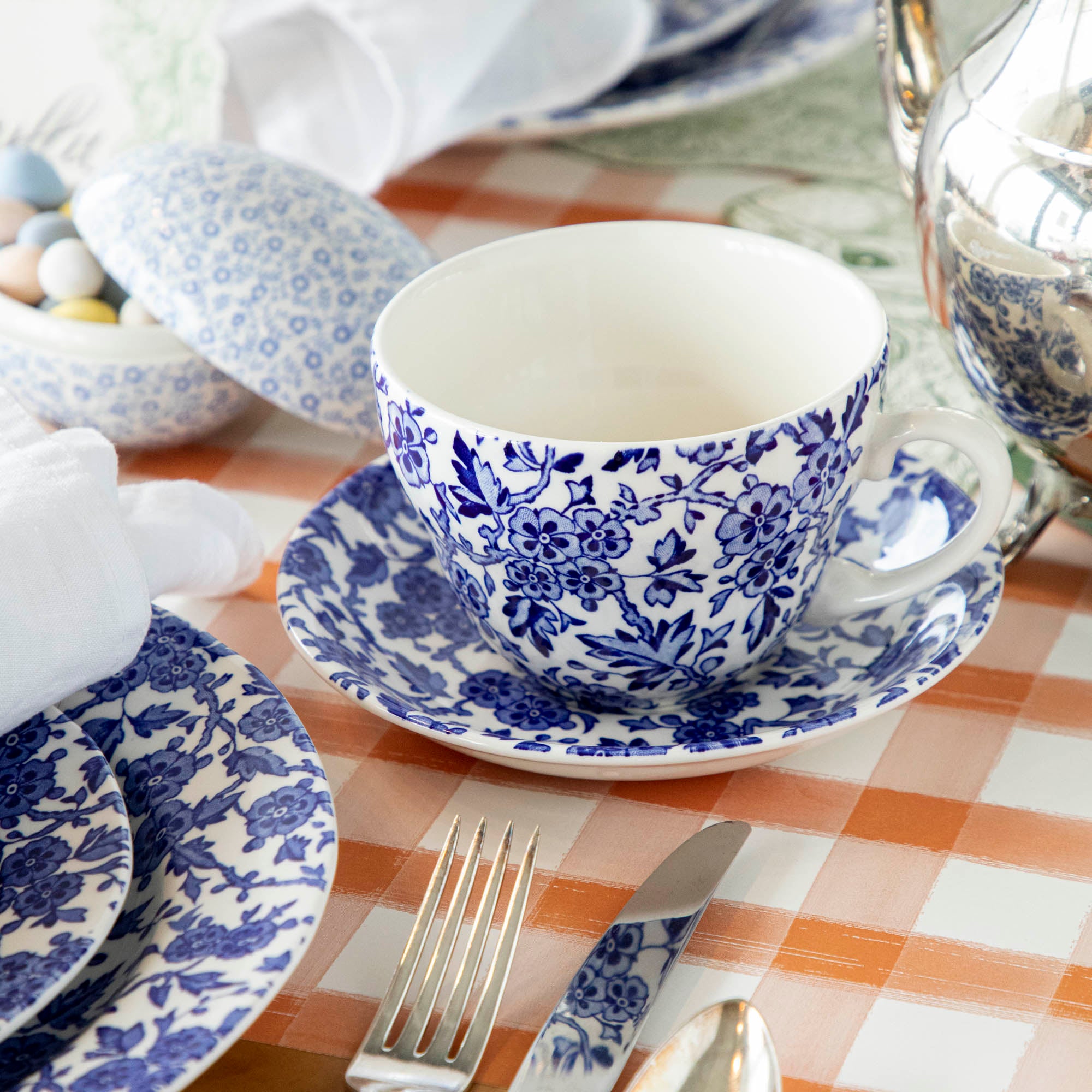 A Burleigh Blue Arden dinnerware plate on a wicker placemat with a folded napkin and a fork to the side, also noted as dishwasher safe.