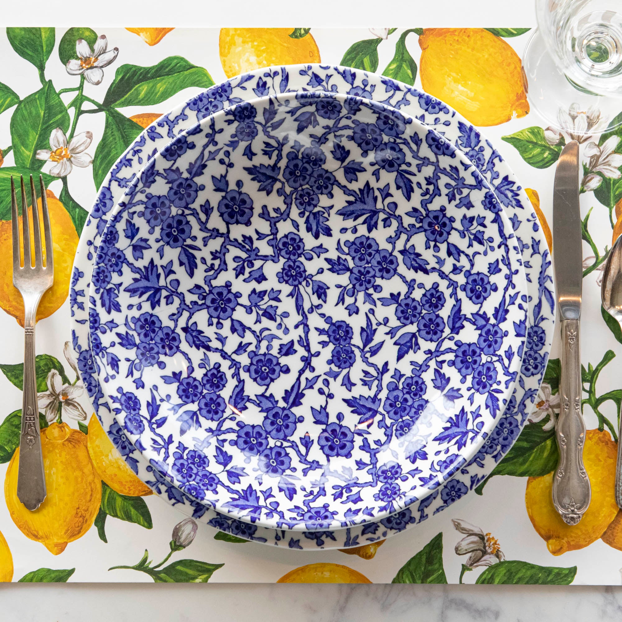 A Burleigh Blue Arden dinnerware plate on a wicker placemat with a folded napkin and a fork to the side, also noted as dishwasher safe.
