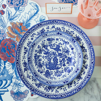 Blue and white patterned Burleigh Blue Regal Peacock Dinnerware plates on a floral patterned background with a name card and a pink glass vase.