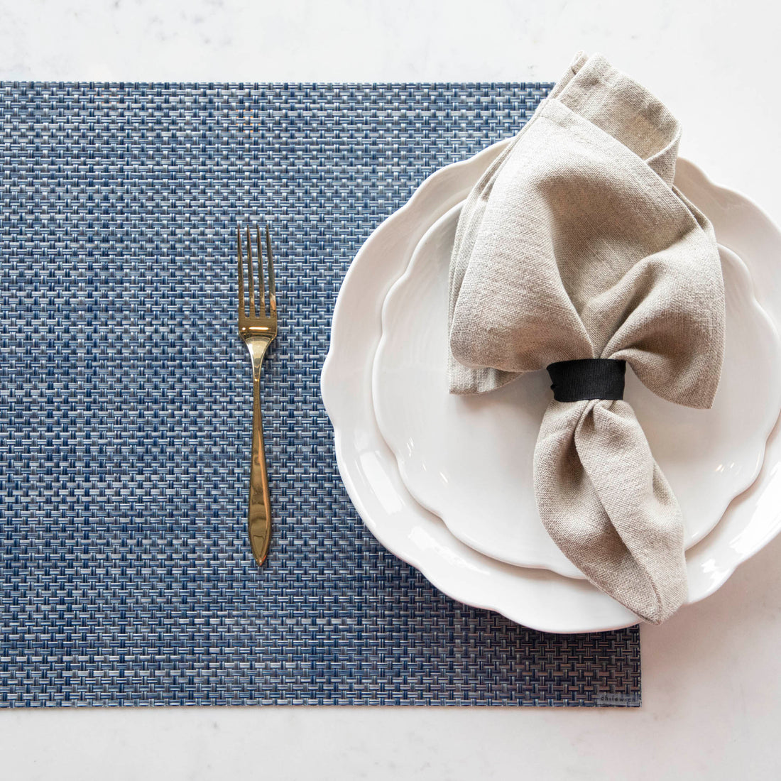 A Chilewich Basketweave Table Mat with a napkin and fork on a table.