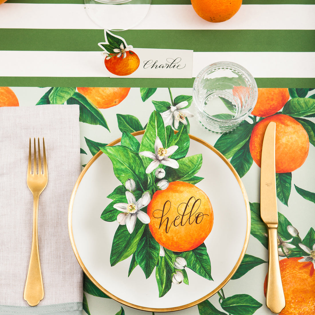 A vibrant citrus-themed place setting featuring an Orange Blossom Table Accent with &quot;hello&quot; written on the orange in beautiful script resting on the plate.