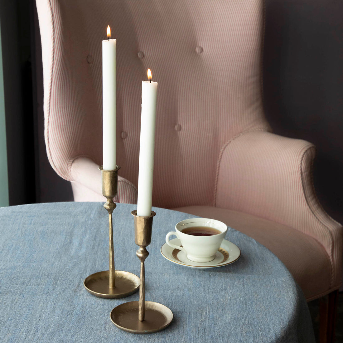 Two Percy Candlestick Brass Plated holders on a table beside a standard size cup of tea with a saucer.