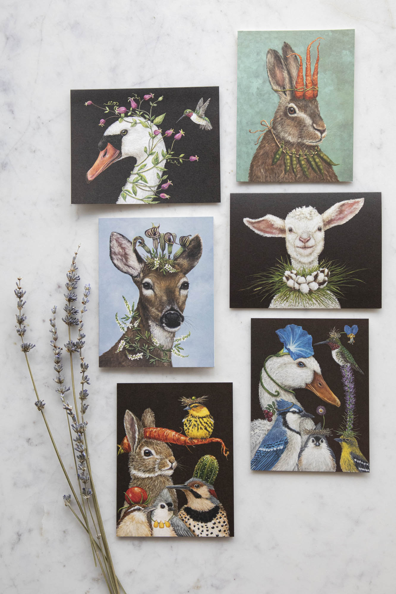 A set of six colorful greeting cards featuring illustrated animals with human-like accessories and expressions, displayed on a marble surface with a sprig of lavender to the side.