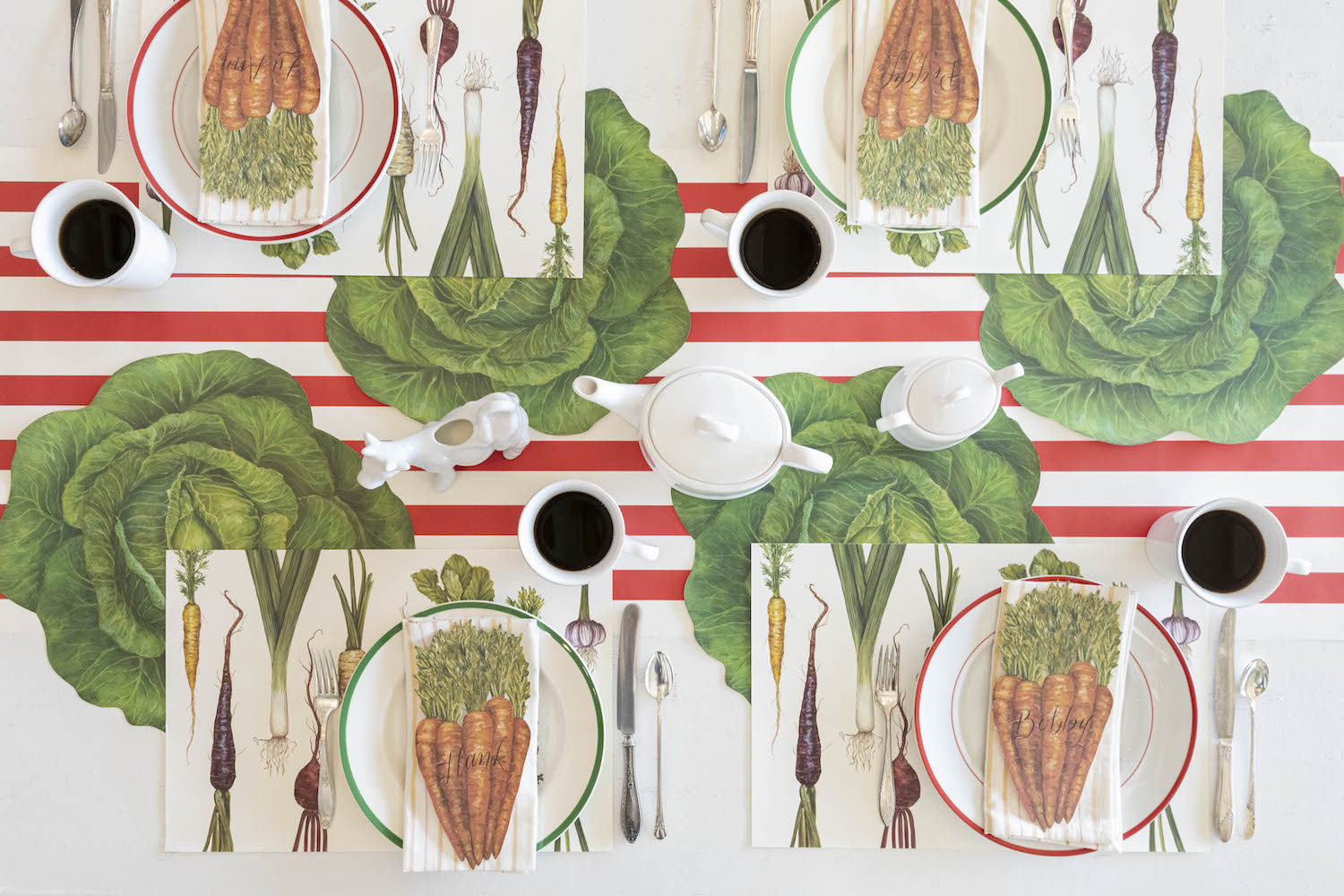 A vegetable-themed table setting featuring Carrots Table Accents resting on each plate with names written on them, from above.