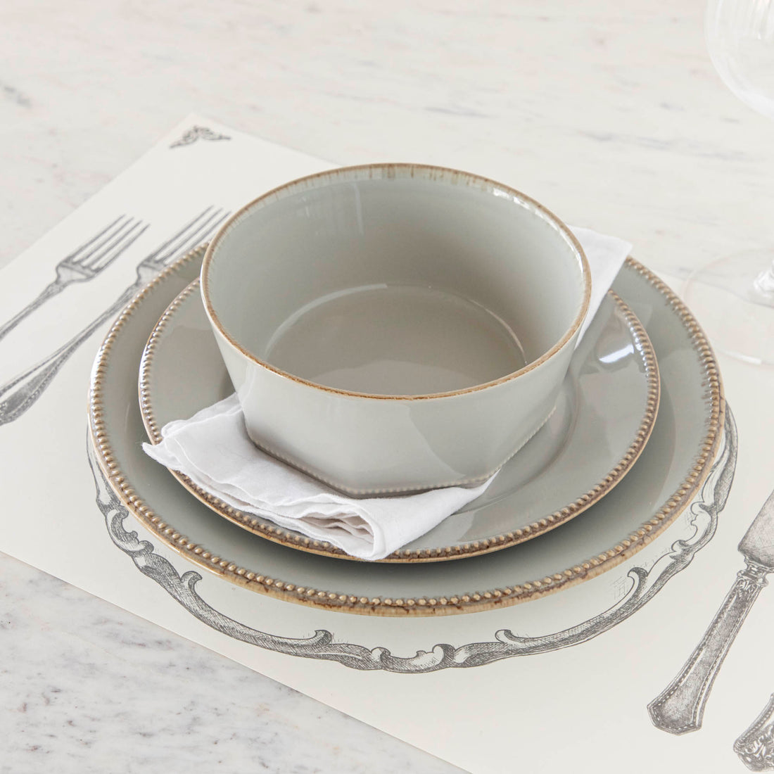 A set of fine stoneware plates and bowls from the Luzia Ash Grey Round Dinnerware collection by Costa Nova on a white surface, perfect for a modern table setting.