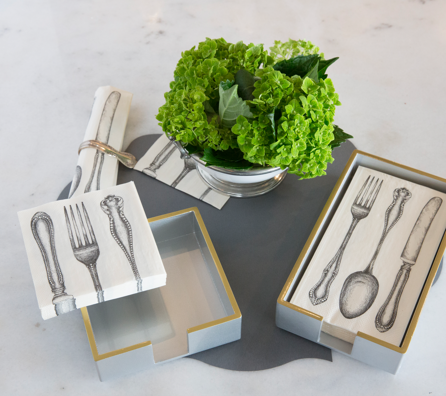 An elegant tablescape featuring a stack of Classic Cutlery Cocktail Napkins sitting on the edge of a white and gold napkin holder, and a stack of Classic Cutlery Guest Napkins sitting in a white and gold napkin holder.