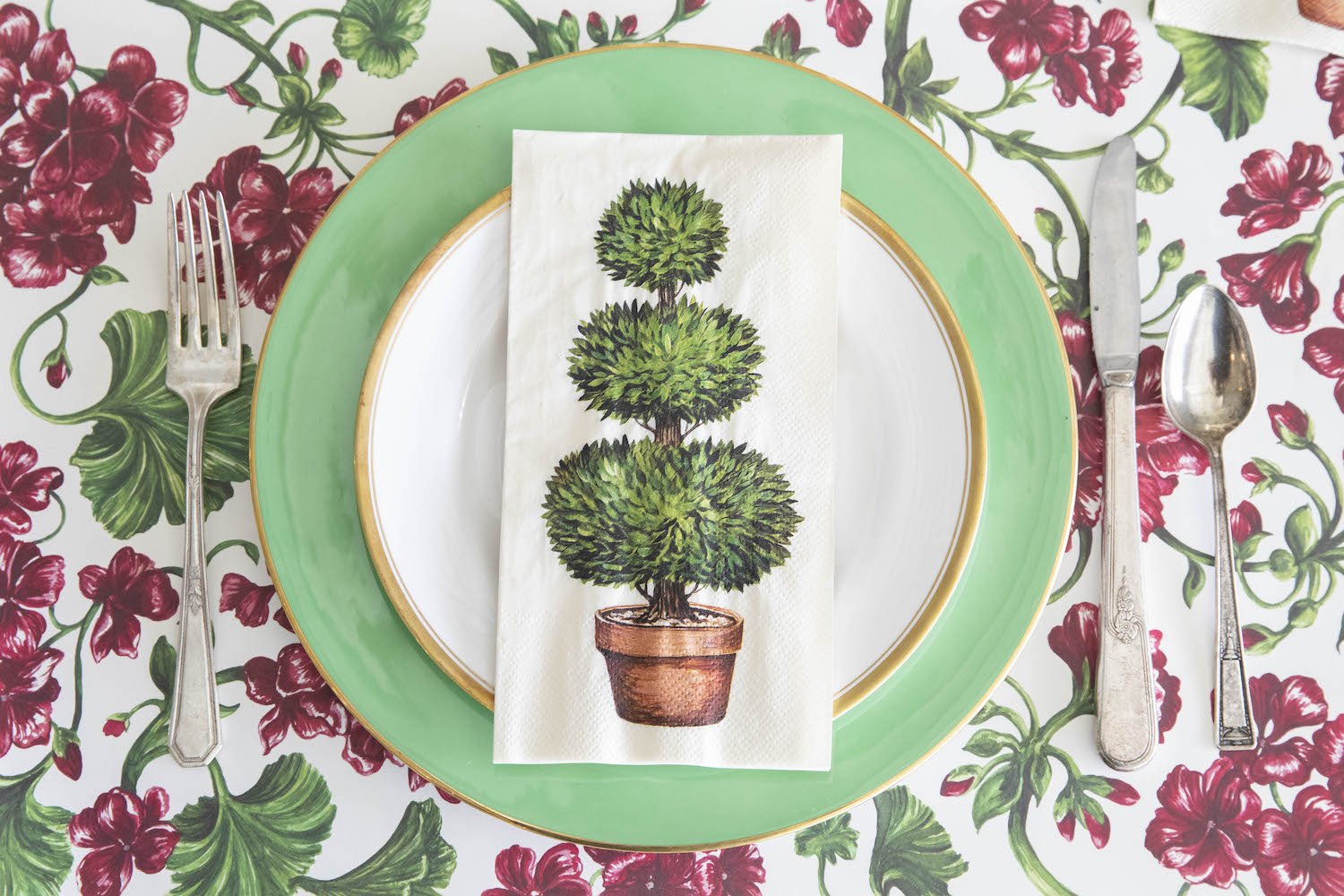 A Topiary Guest Napkin centered on the plate of a garden-themed place setting, from above.