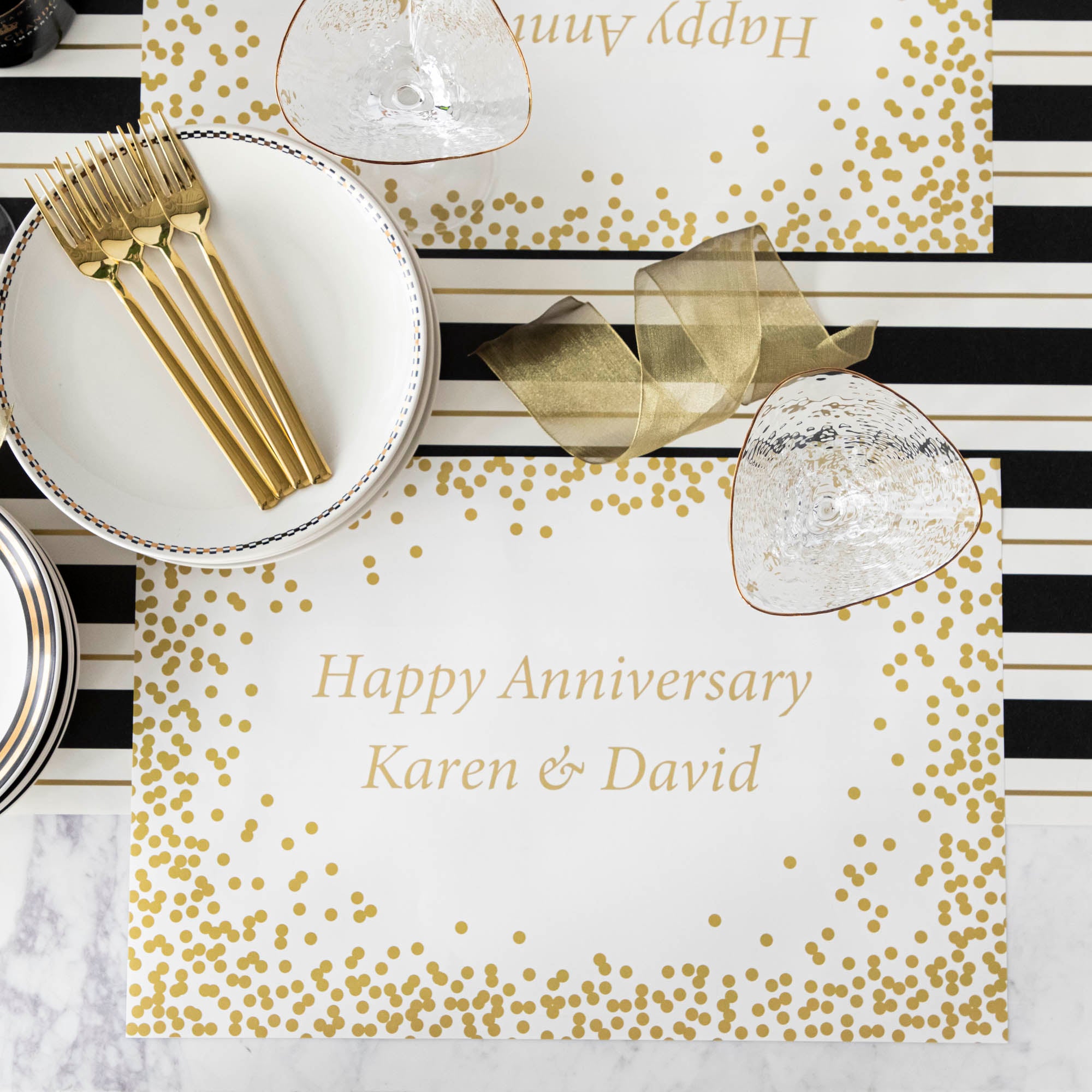 Table setting with Gold Confetti Placemat with personalized message printed in gold color: "Happy Anniversary Karen & David".