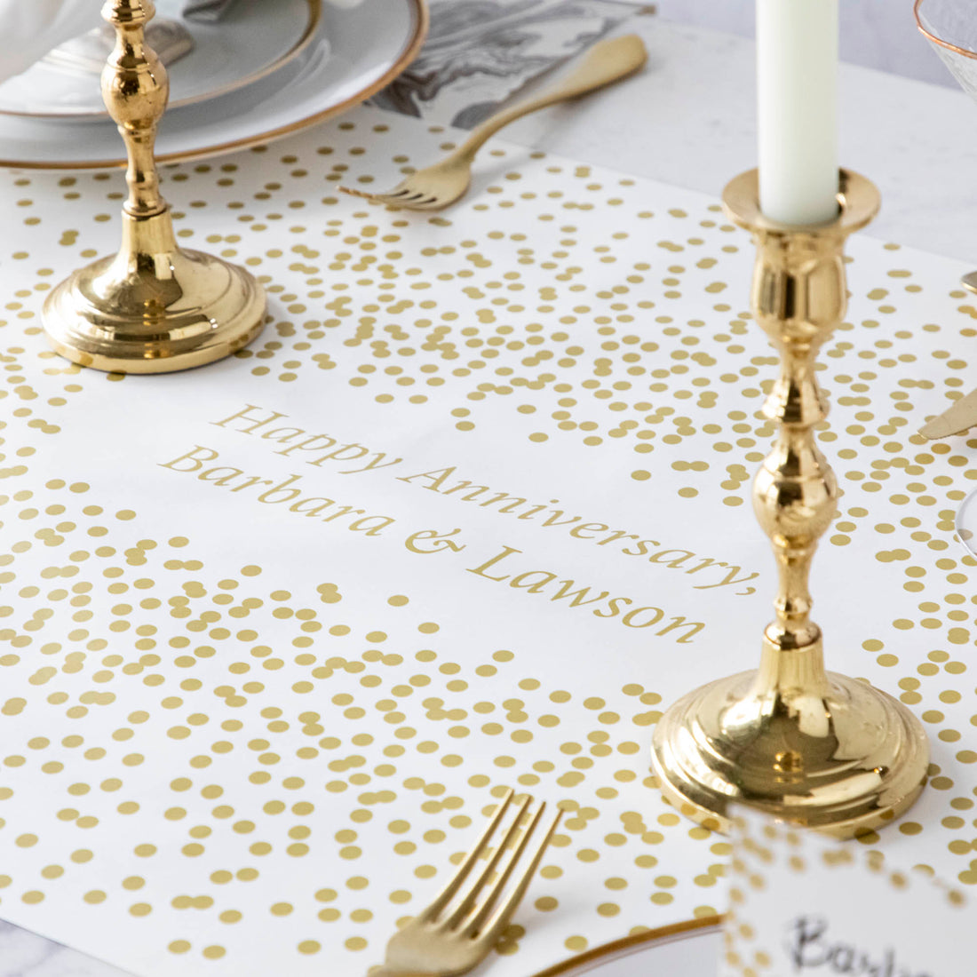 The Gold Confetti Personalized Runner under an elegant table setting, with &quot;Happy Anniversary, Barbara &amp; Lawson&quot; printed in gold in the center.
