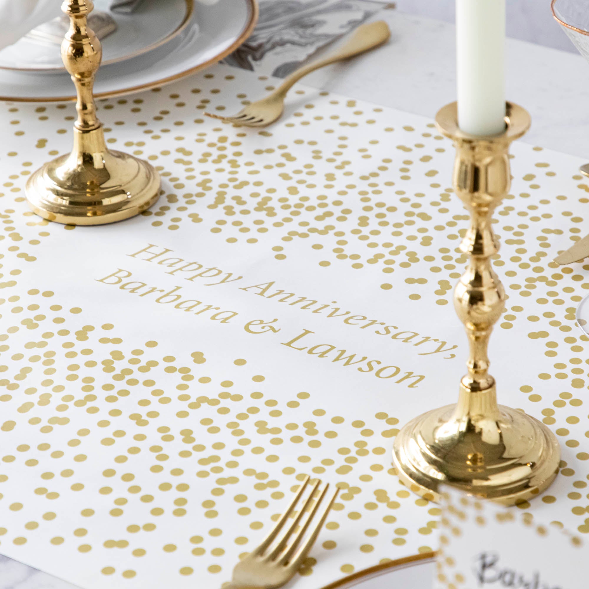 The Gold Confetti Personalized Runner under an elegant table setting, with "Happy Anniversary, Barbara & Lawson" printed in gold in the center.