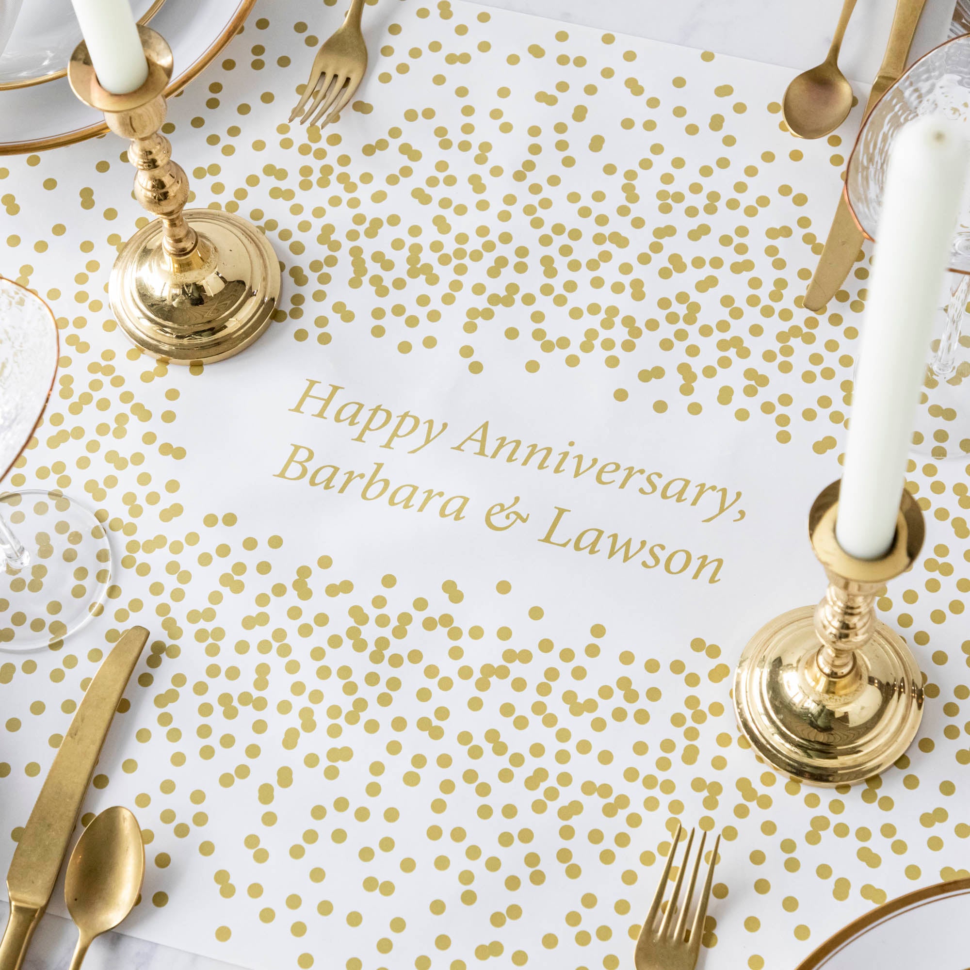 The Gold Confetti Personalized Runner under an elegant table setting, with "Happy Anniversary, Barbara & Lawson" printed in gold in the center.