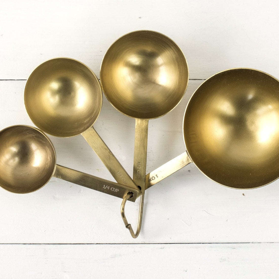 Set of Be Home brass measuring cups on a white wooden surface.