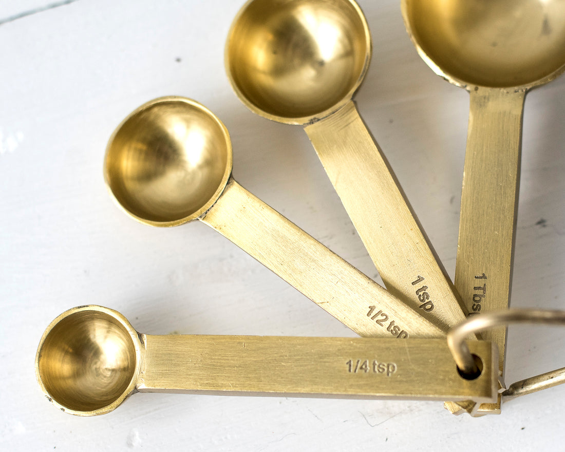 A set of ethically crafted Be Home brass measuring spoons with a food-safe coating on a wooden surface.