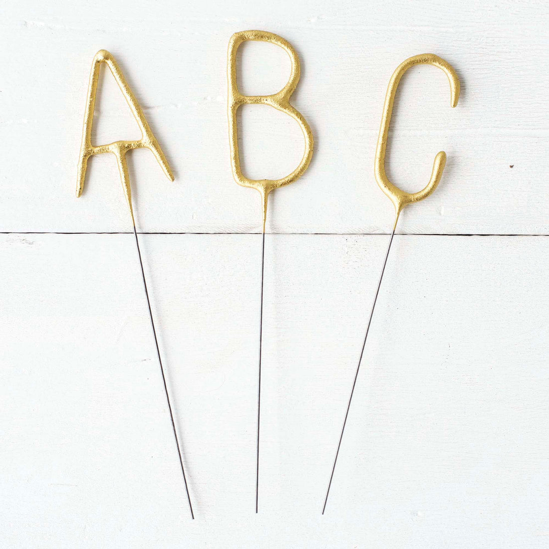 Three Tops Malibu gold Letter Sparklers on a wooden surface.