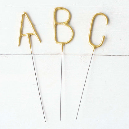 Three Tops Malibu gold Letter Sparklers on a wooden surface.