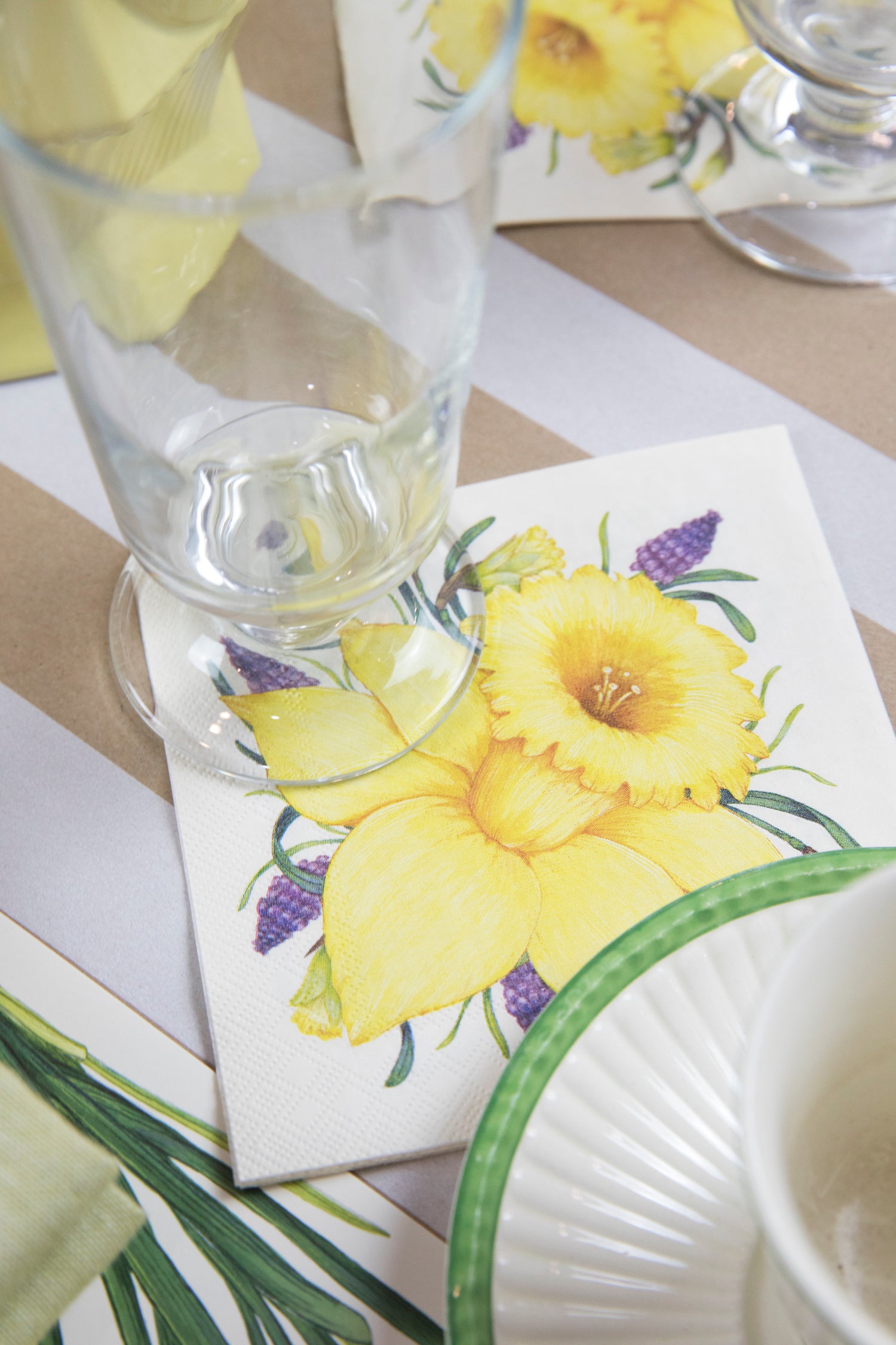 A Daffodil Cocktail Napkin under a water glass in an elegant place setting.