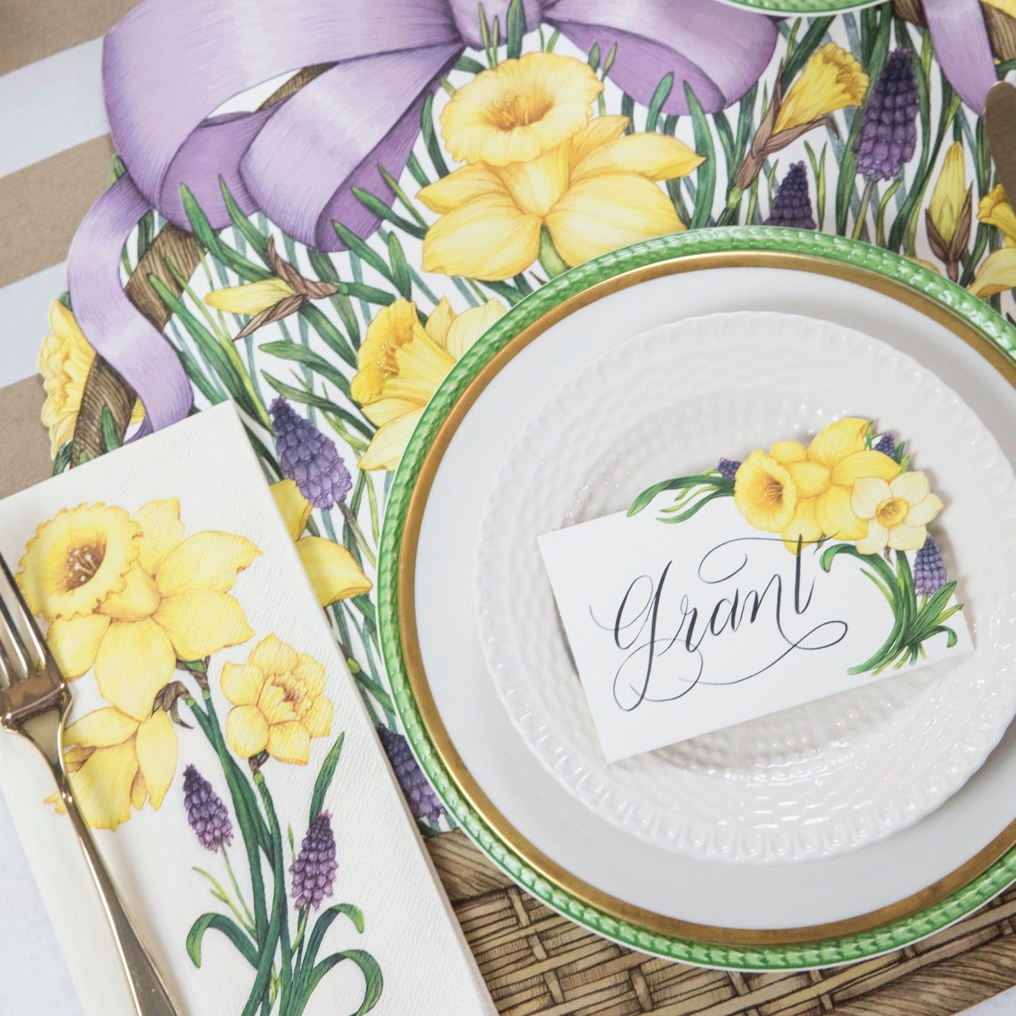 A Hester & Cook Daffodil Place Card labeled "Grant" laying flat on a plate in an elegant place setting.