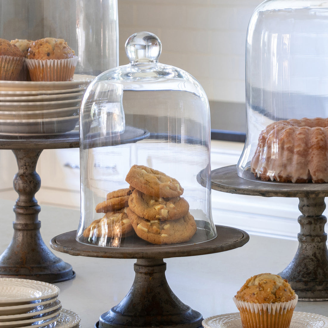Glass-domed Park Hill cake stands, resembling bell jars, displaying baked goods on a table.