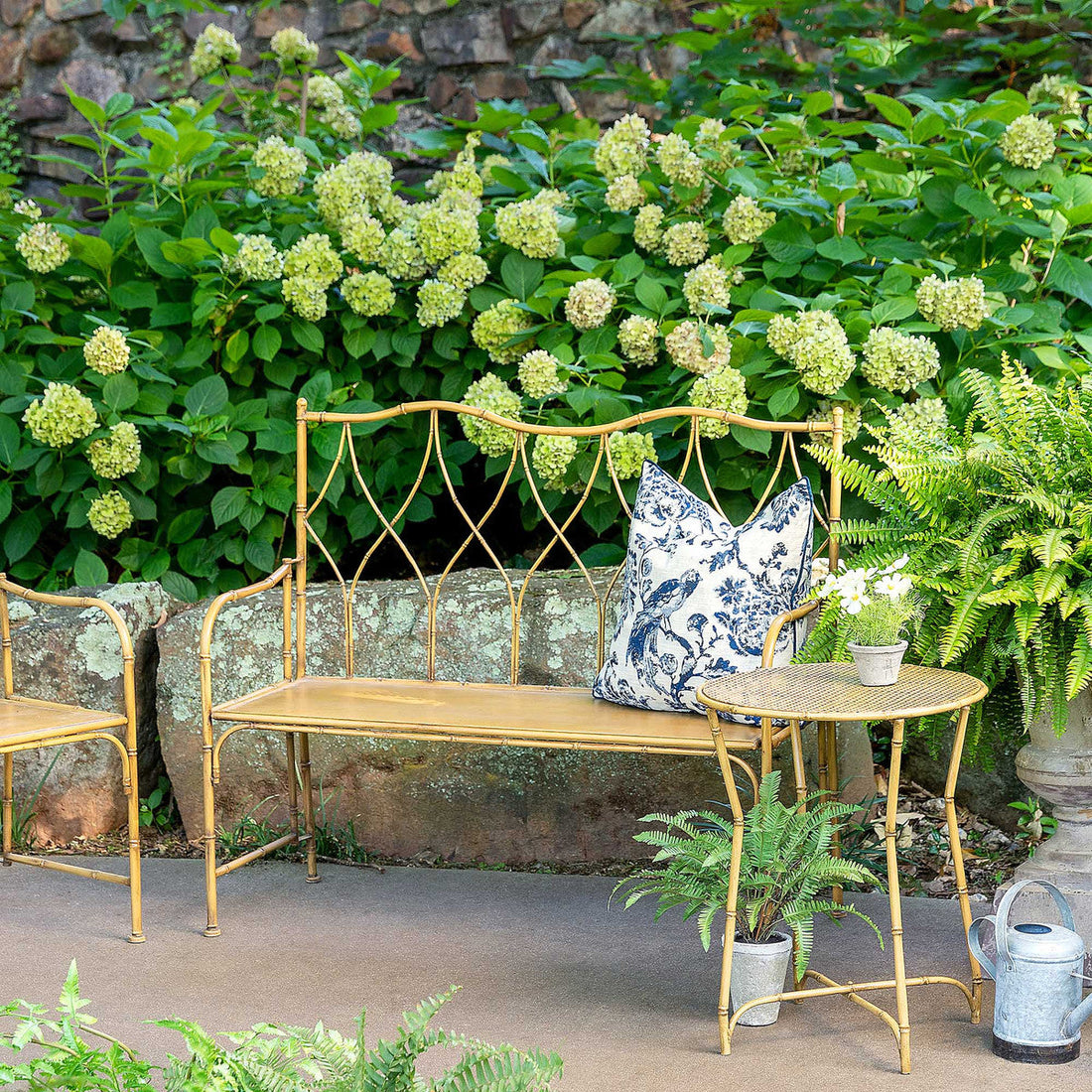 A cozy garden nook with a Park Hill Metal Bamboo Porch Bench, cushions, a side table, and lush greenery.