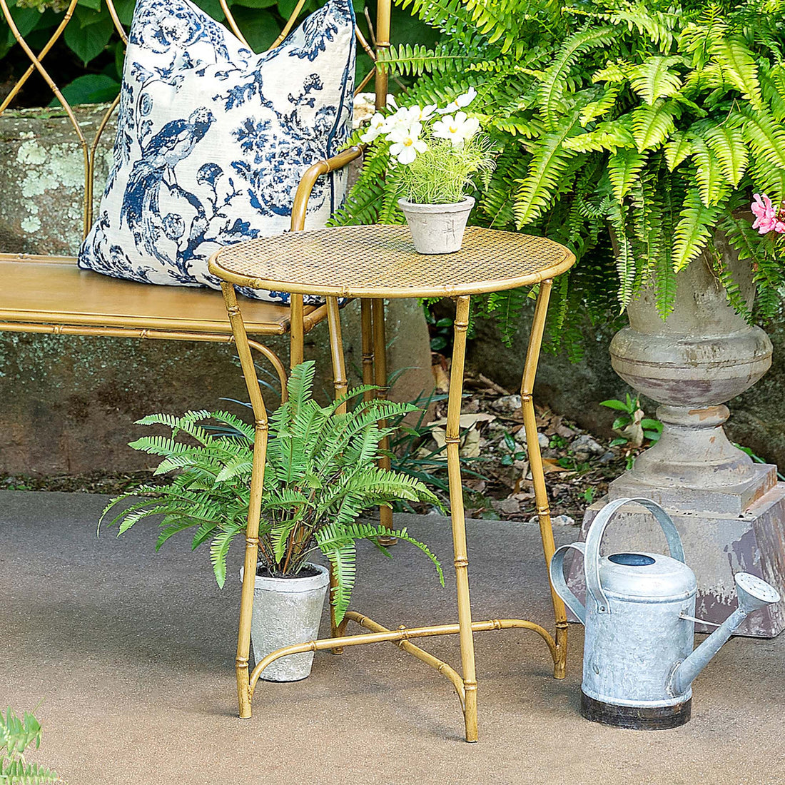 A cozy outdoor sitting area with Park Hill metal bamboo side pieces, a round table, potted plants, and a watering can.