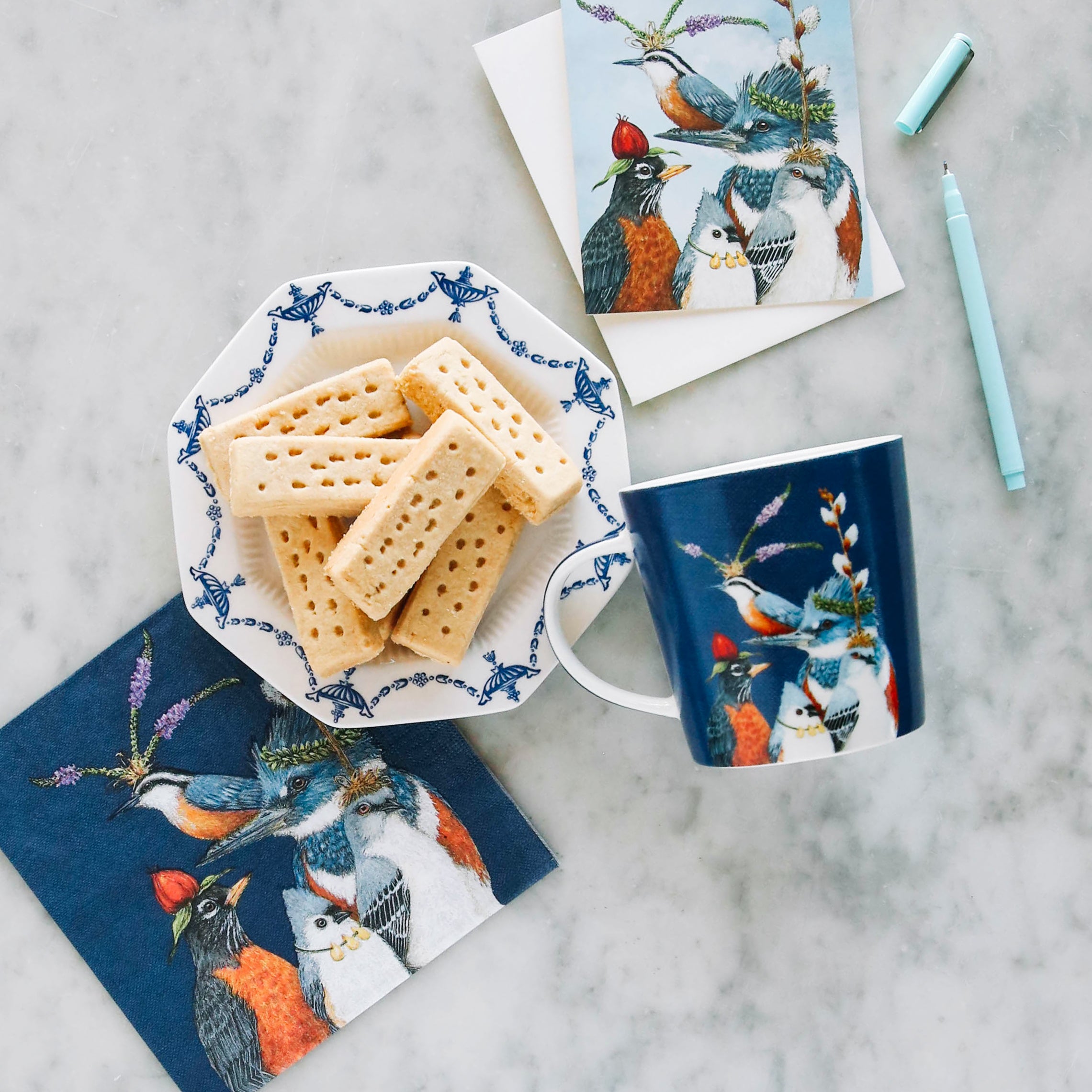 The gift mug on a table with matching napkin and card, next to a plate of cookies.