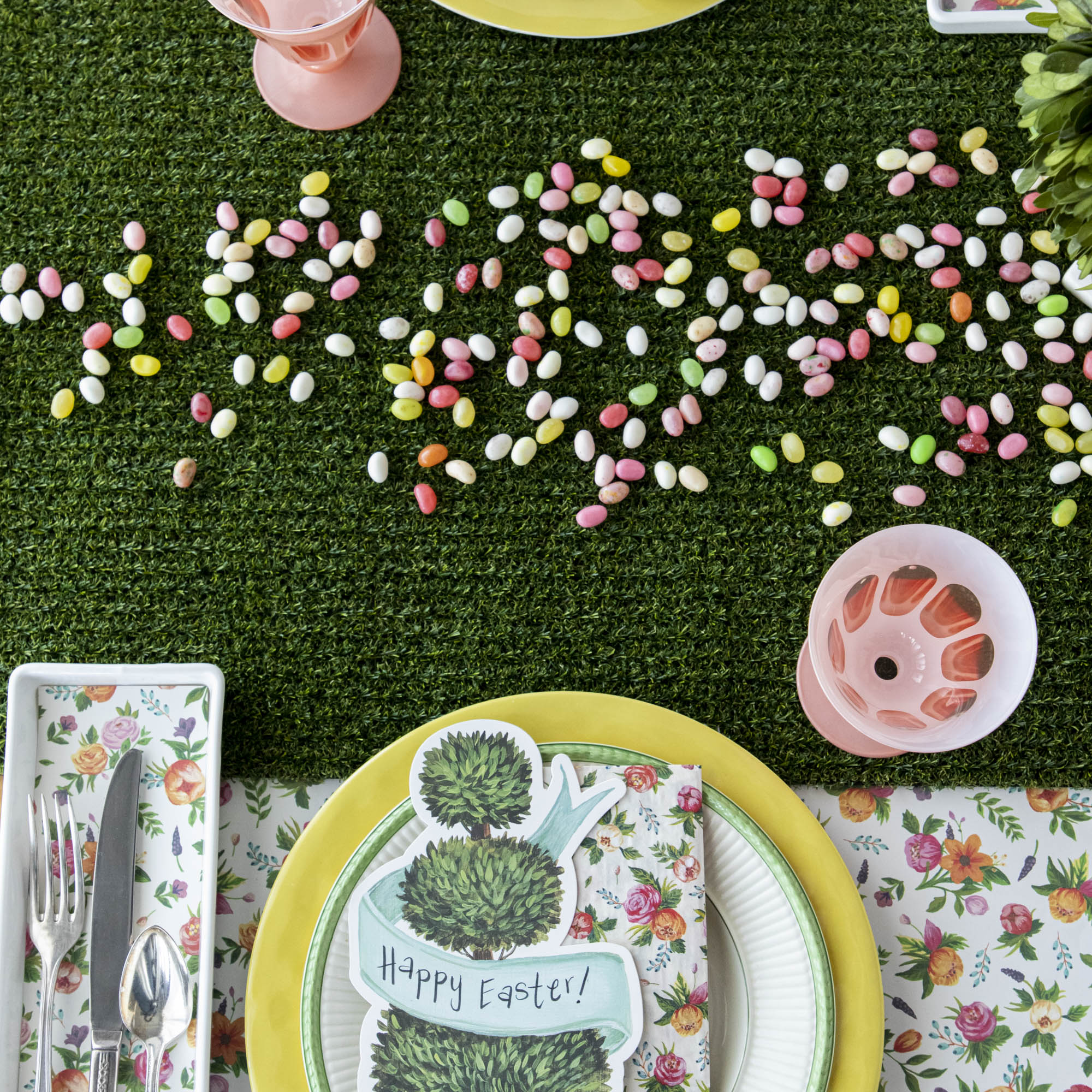 A festive table setting with easter eggs, plates, napkins, and utensils set on a Talking Tables Artificial Grass Table Runner. Perfect for a party celebration!